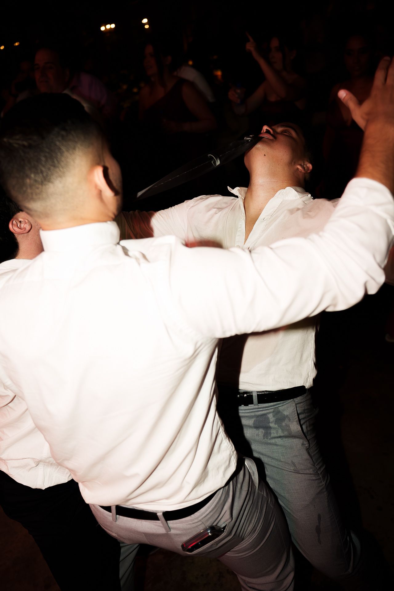 Two men in white shirts performing energetically on stage with a microphone before a dark crowd.