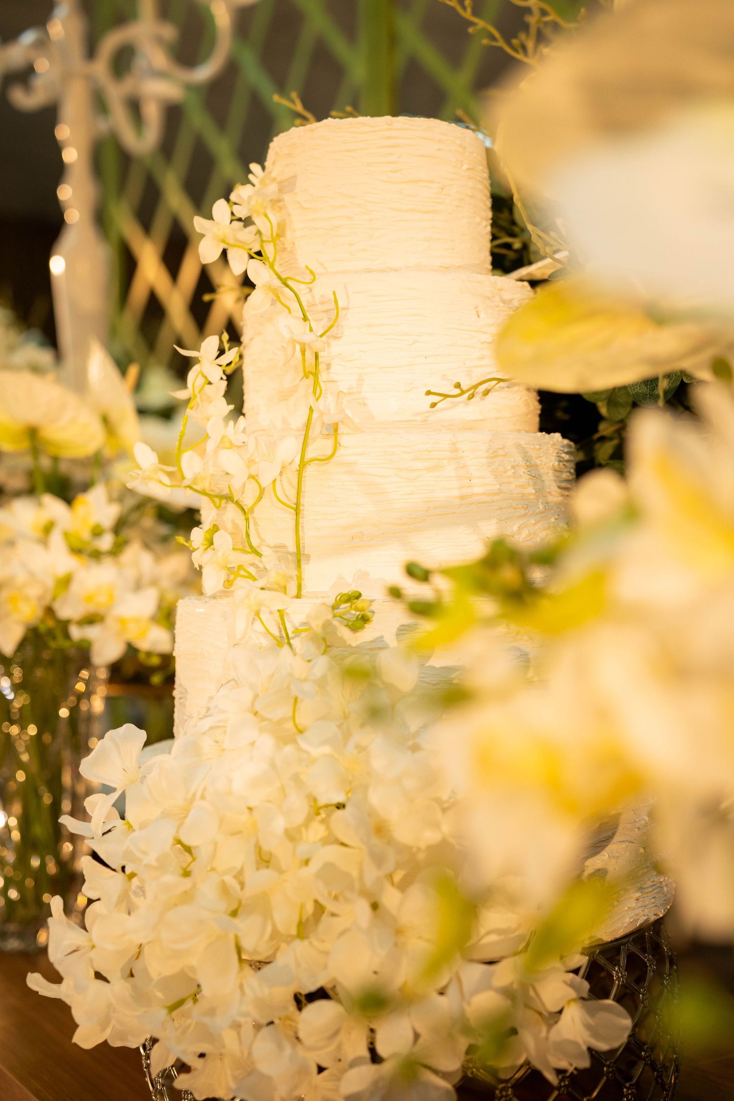 Elegant three-tier white wedding cake adorned with yellow orchids and white flowers on a decorated table.