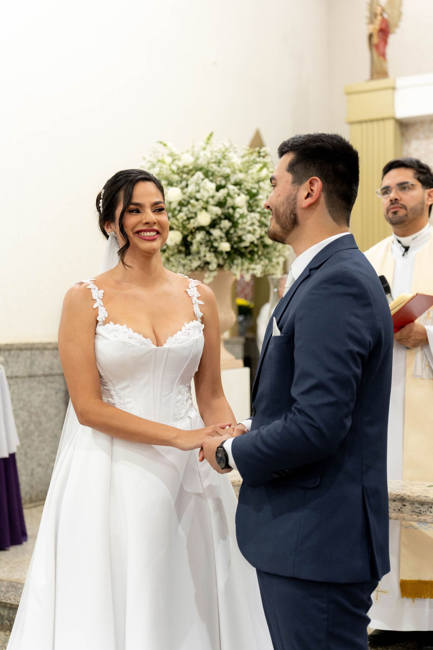 Bride and groom exchange vows at church altar, smiling joyfully, with officiant holding book in background.