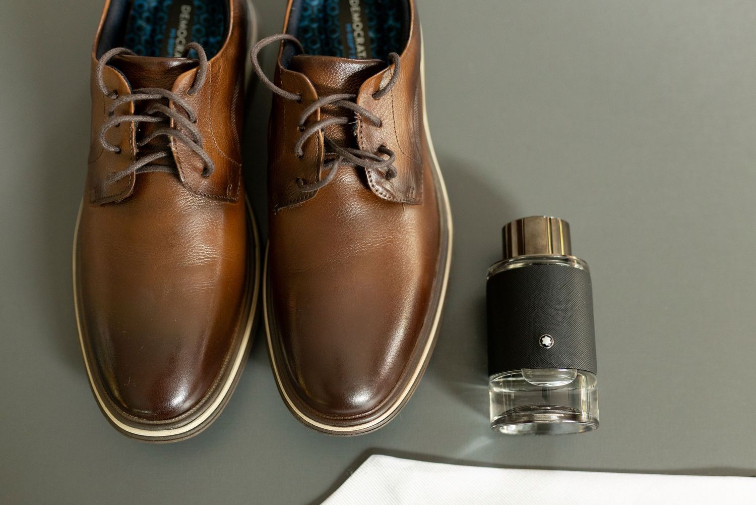Brown leather lace-up dress shoes displayed next to a Montblanc cologne bottle on a gray surface.