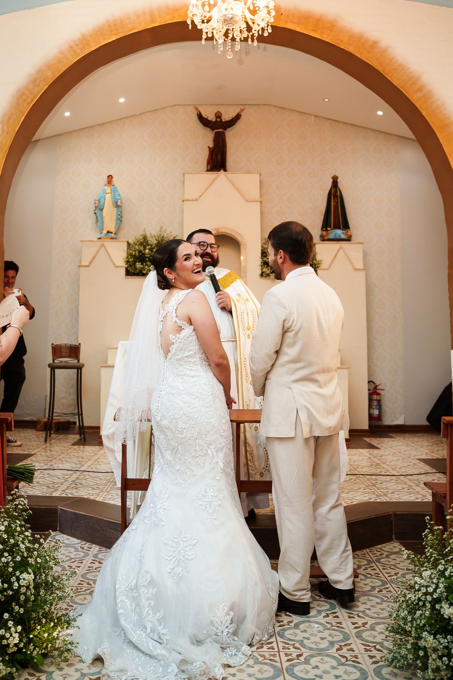 Bride and groom exchange vows at a Catholic church altar, bride in lace mermaid gown with veil.