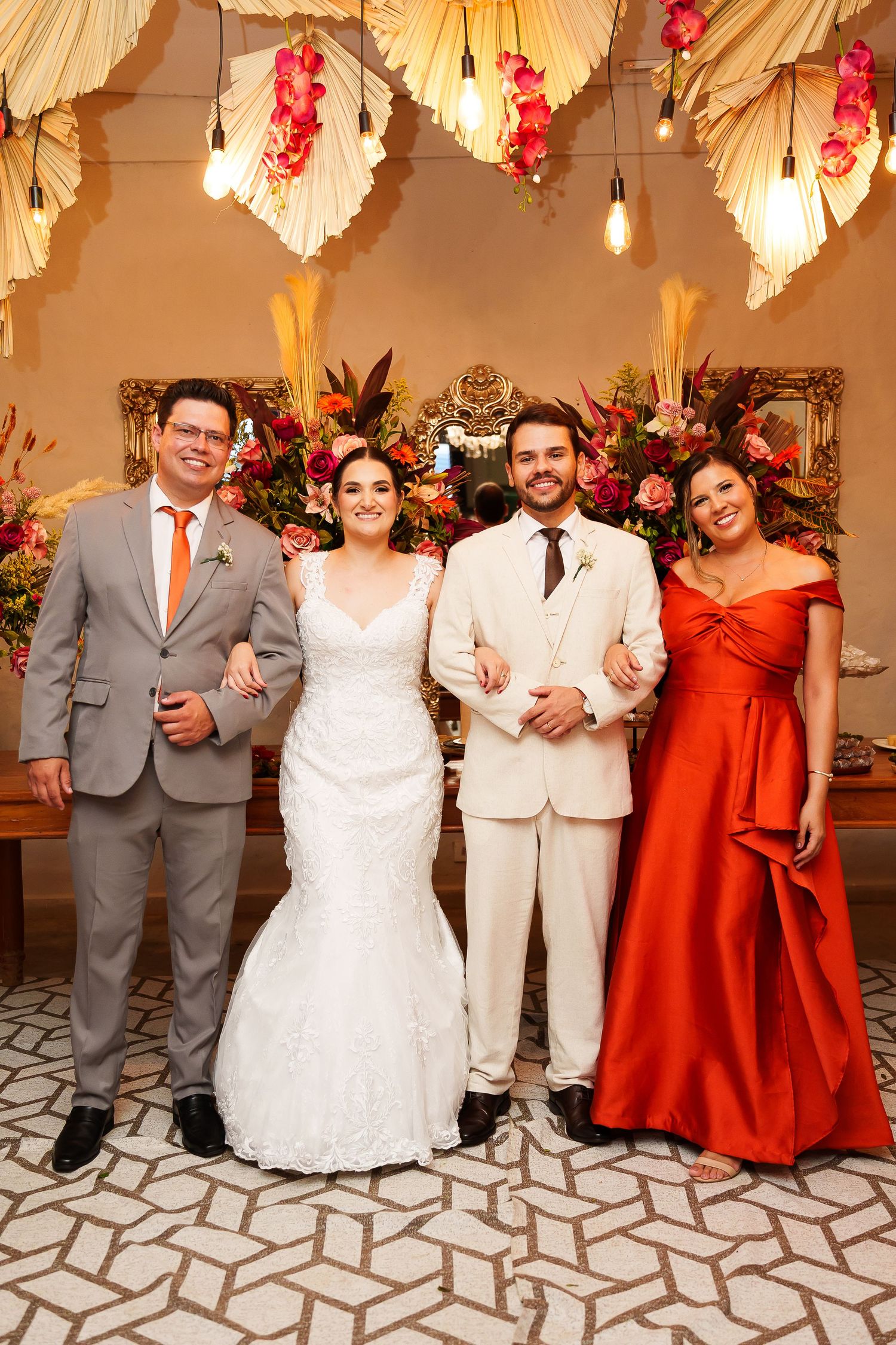 Bride and groom pose with two guests at elegant wedding reception with tropical floral decor and warm lighting.