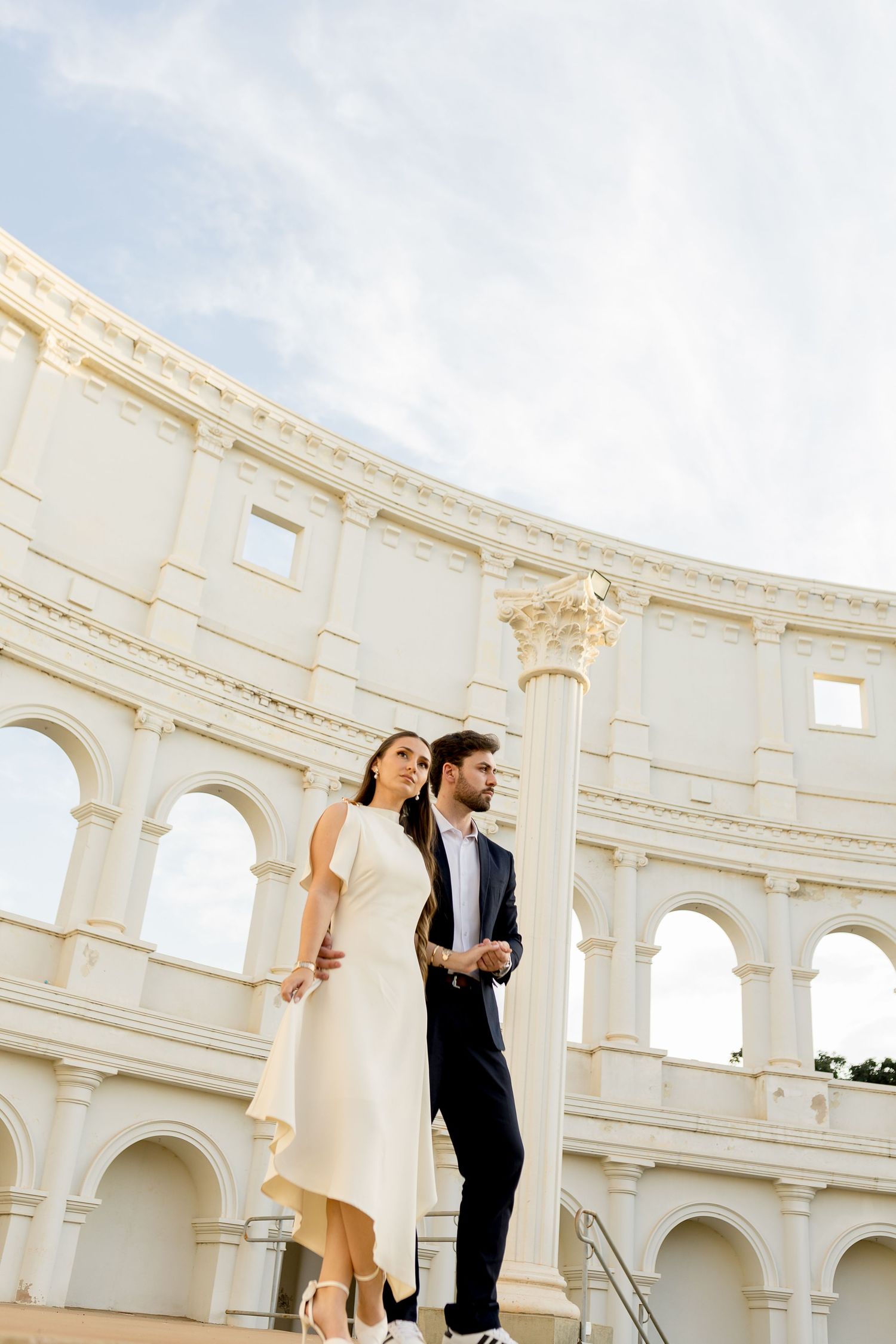 Elegant couple in formal attire standing before the Roman Colosseum on a sunny day.
