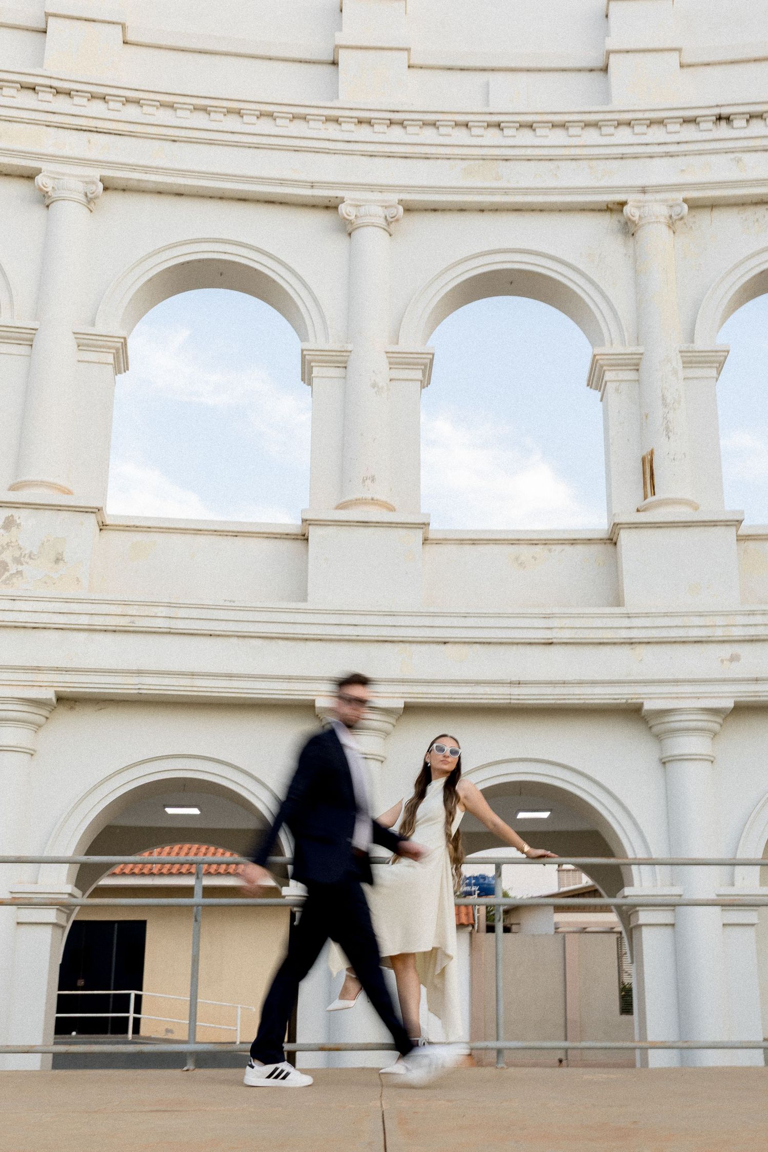 Couple holding hands at white classical architecture building with arched windows, motion blur effect.