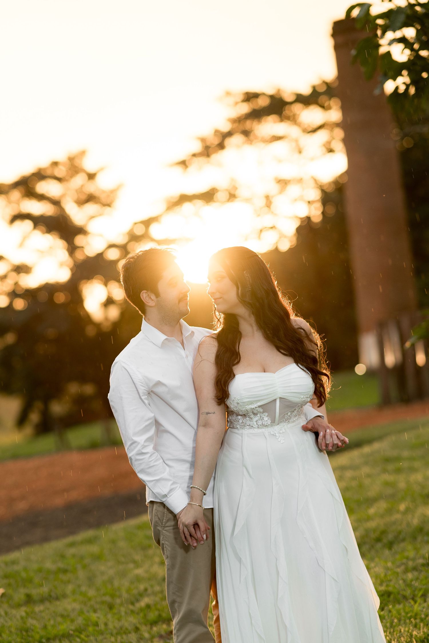 Couple in wedding attire sharing a romantic moment at golden hour sunset in a lush green park.