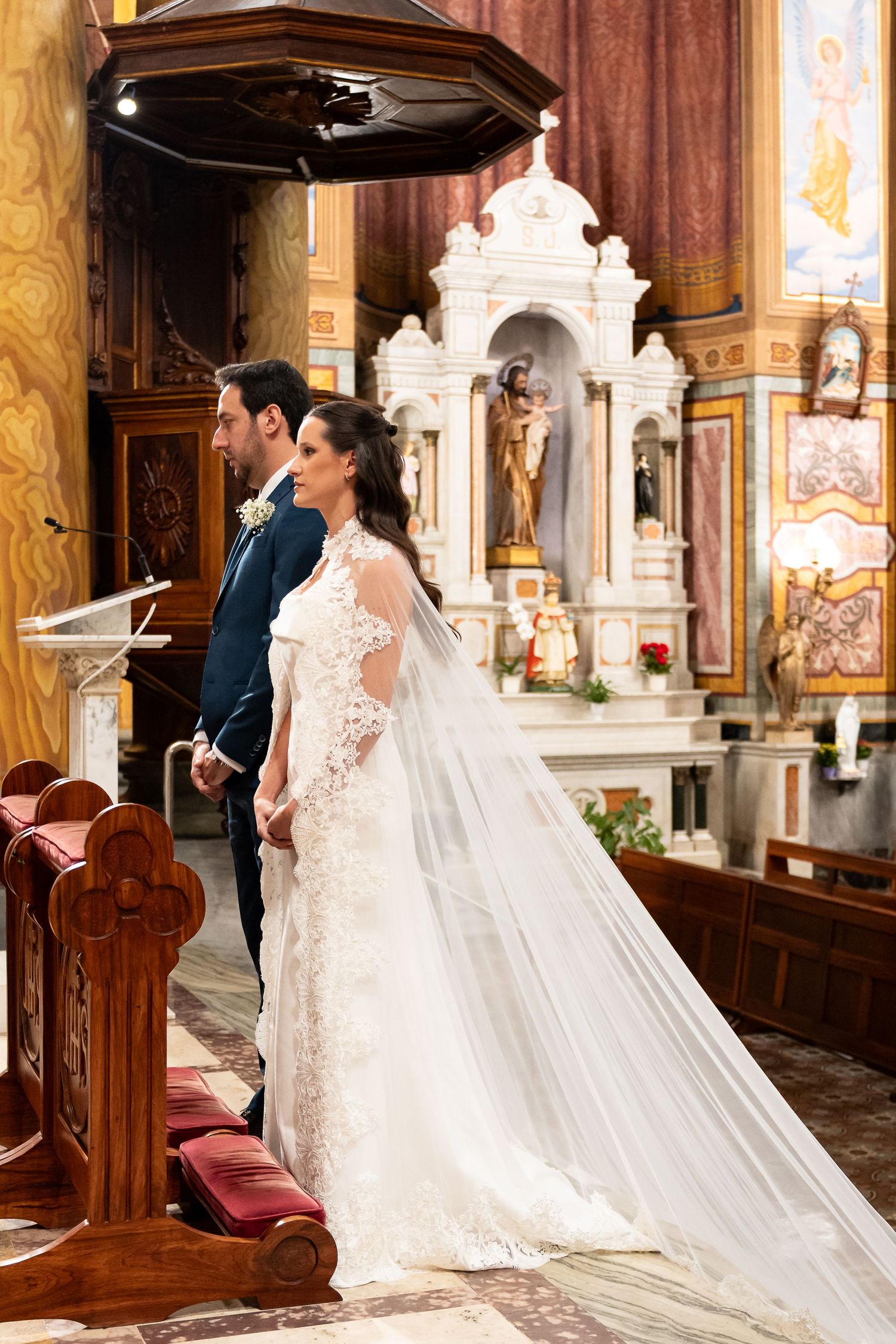 Bride and groom standing at church altar during wedding ceremony, bride wearing lace gown with long veil.