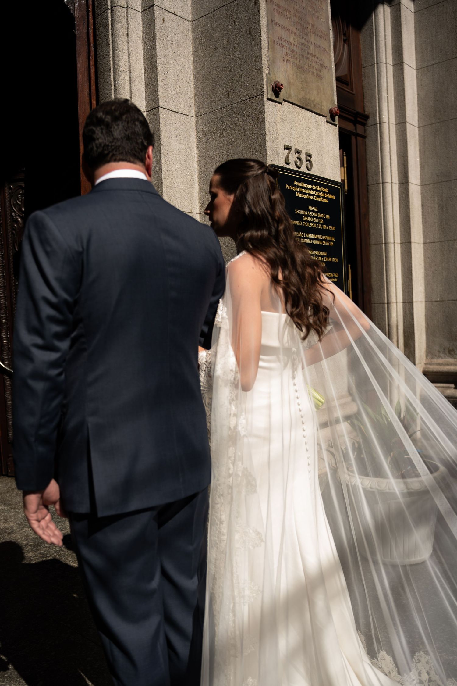 Bride and groom walking hand in hand toward church entrance 735, bride wearing elegant white gown with flowing veil.