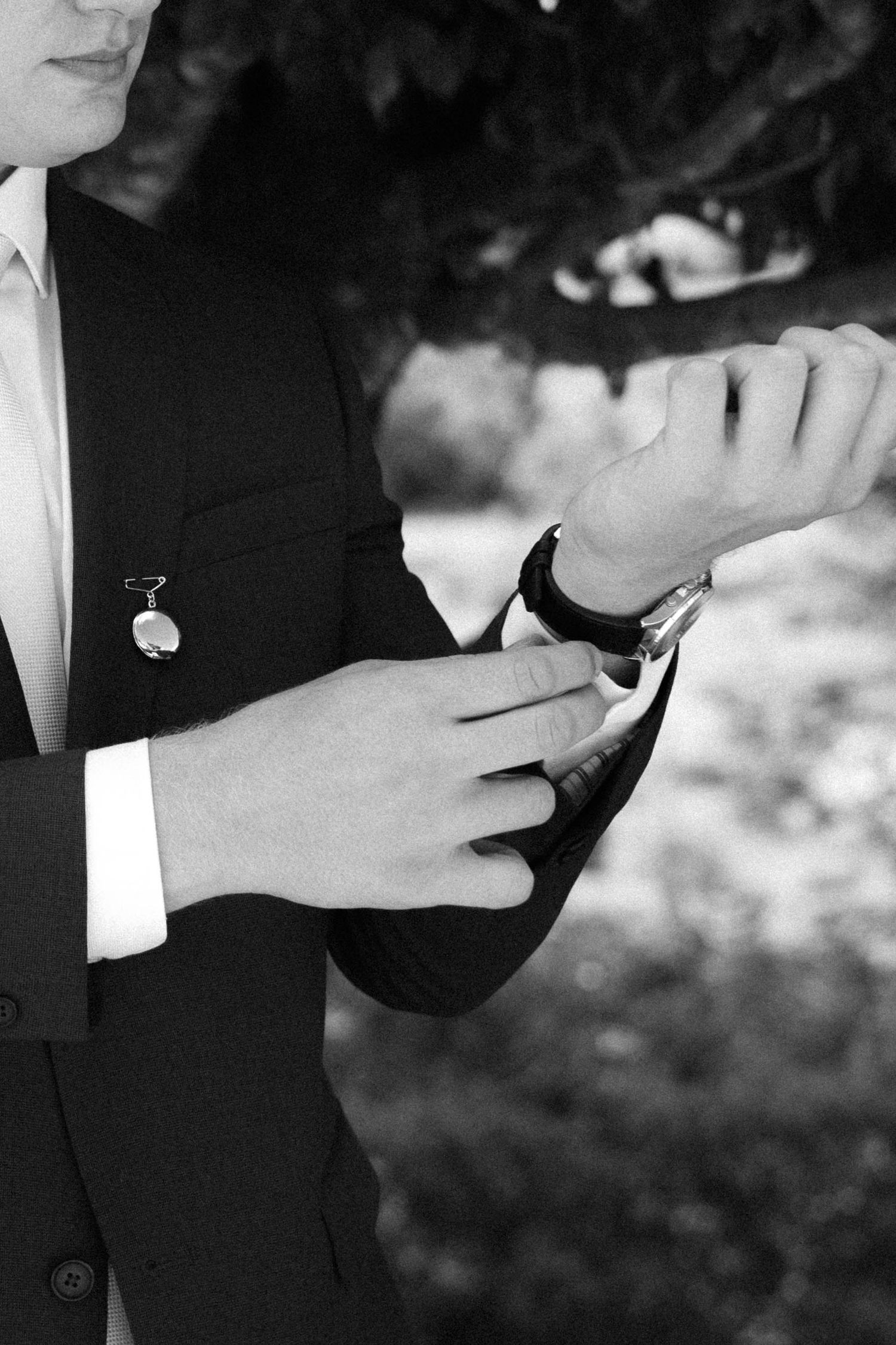 Black and white photo of a groom in a suit adjusting his watch before the wedding ceremony.