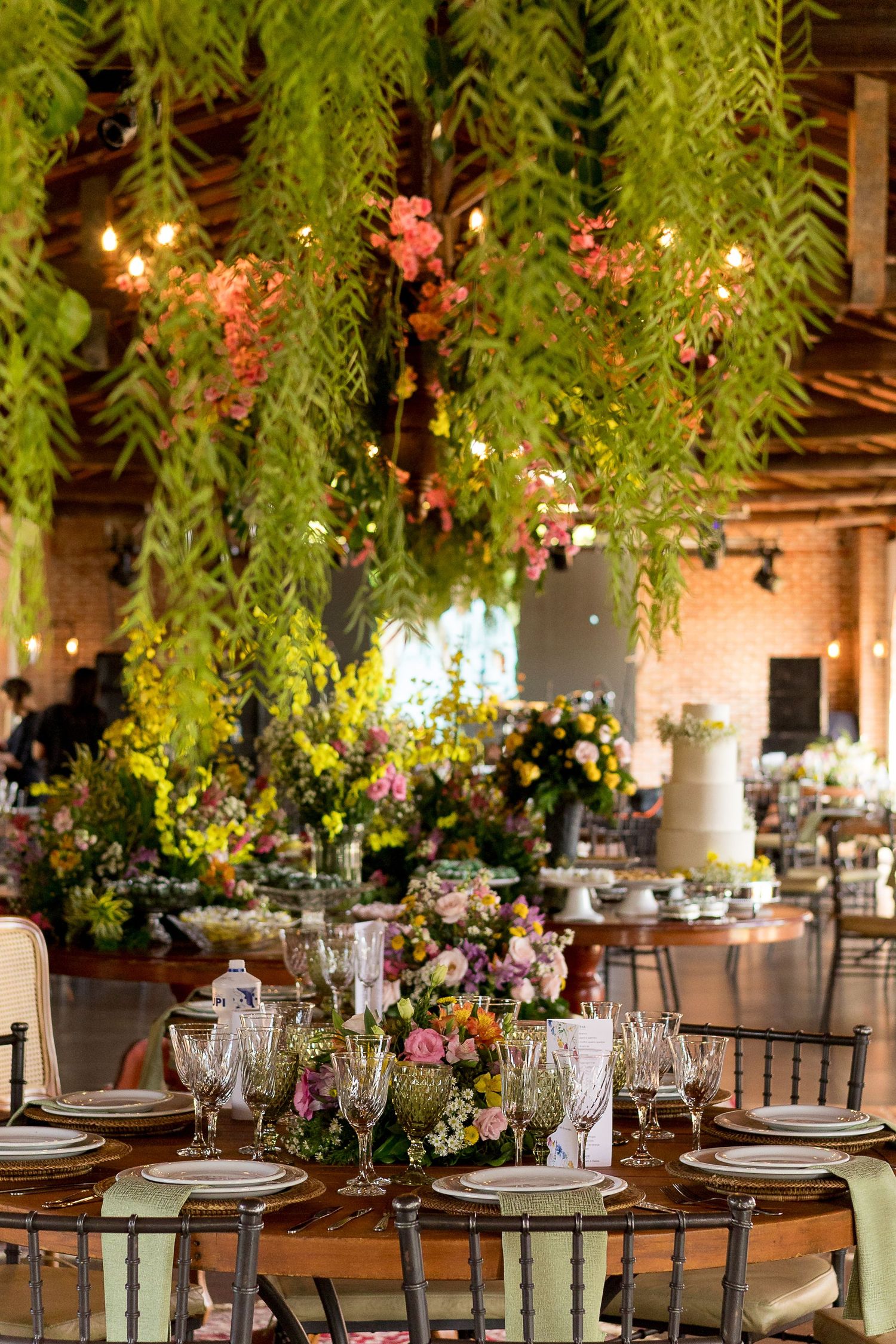 Elegant event venue with hanging greenery, string lights, floral centerpieces, and beautifully set dining tables.