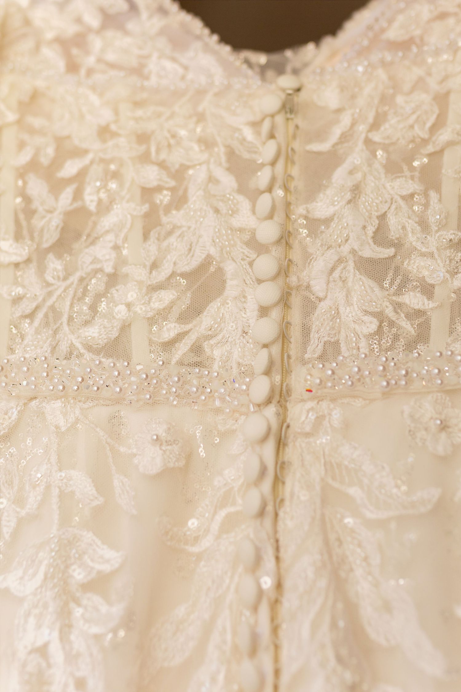 Close-up of ivory wedding dress back with intricate beaded lace applique, pearl buttons, and delicate floral embroidery.