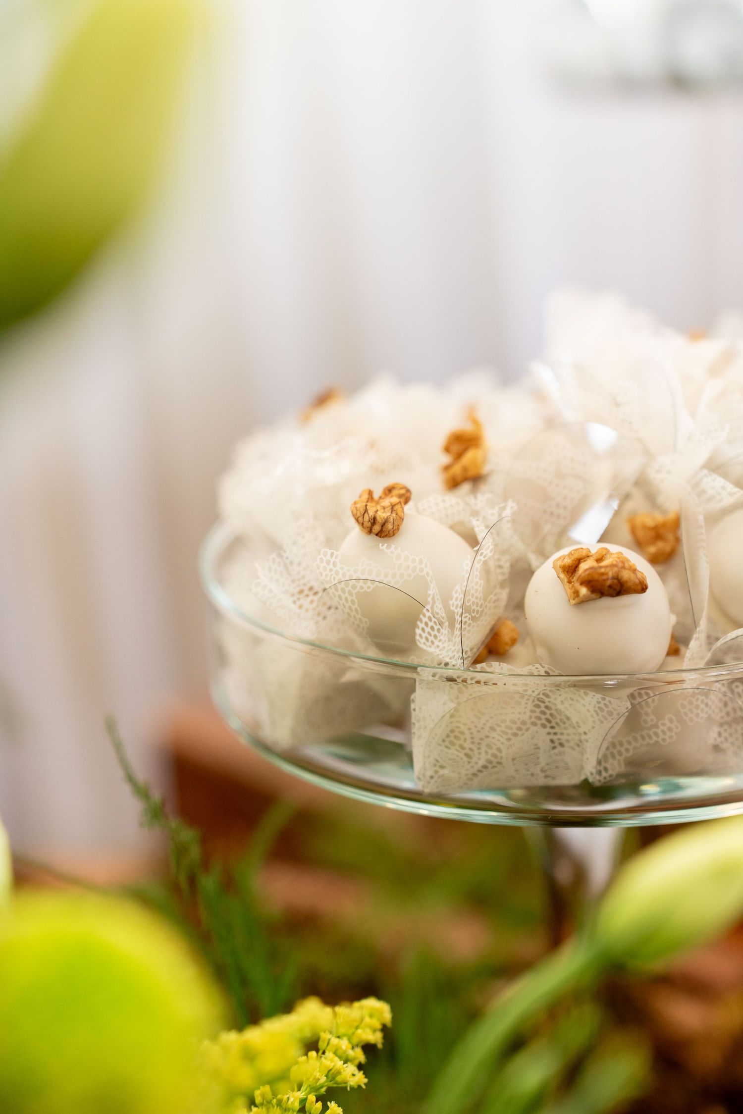 Elegant white chocolate truffles topped with walnuts displayed on a glass cake stand with lace accents.