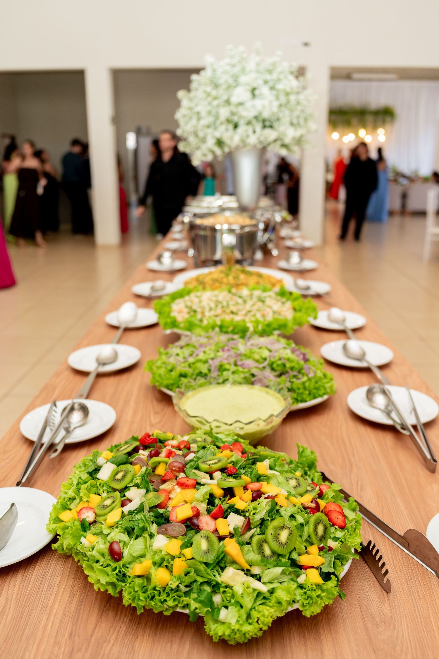 Elegant buffet table with colorful fresh salads, white plates, and floral centerpiece at a formal event.