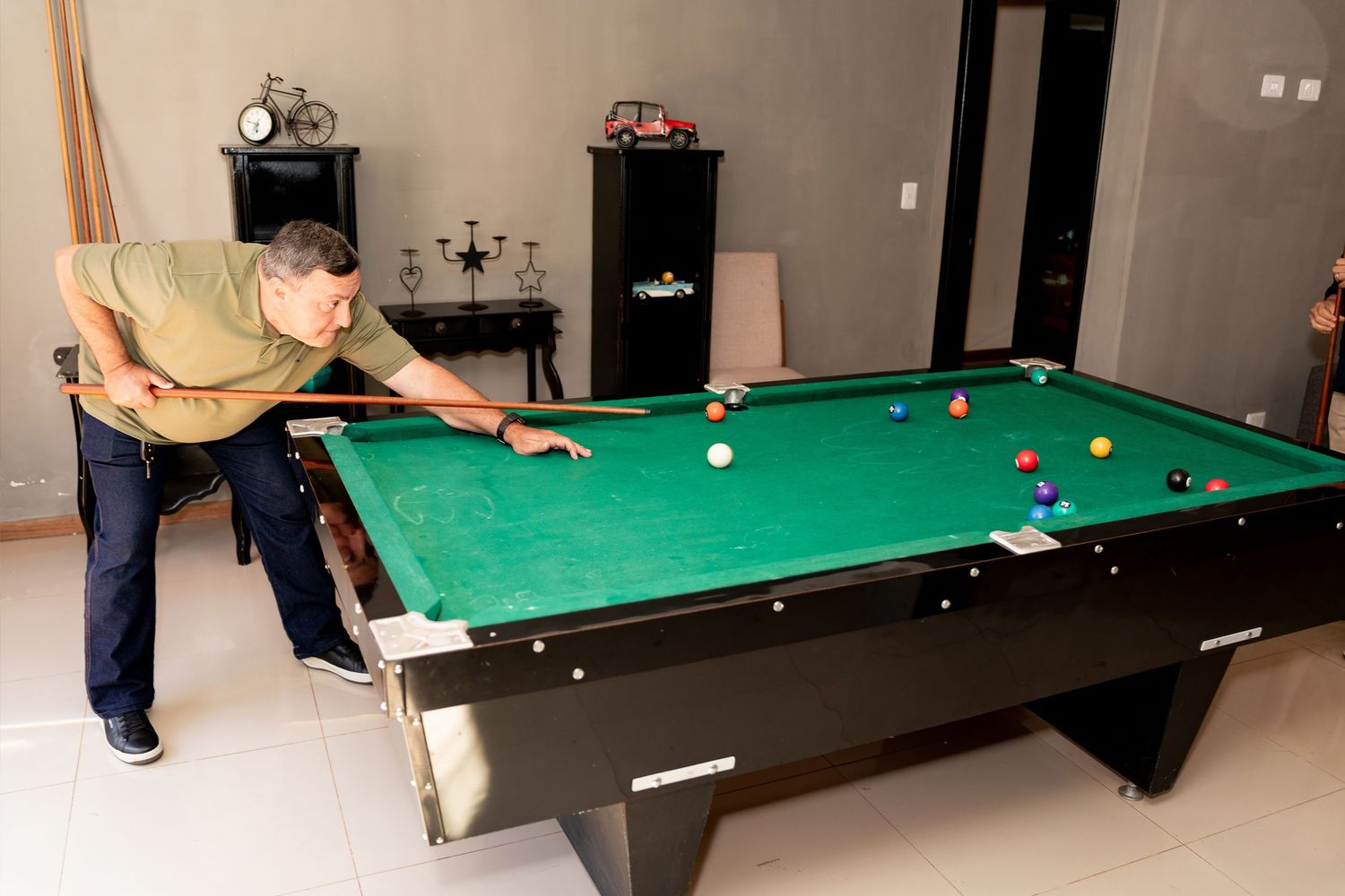 Man playing pool on a green billiard table in a well-lit game room with colorful balls arranged for a shot.