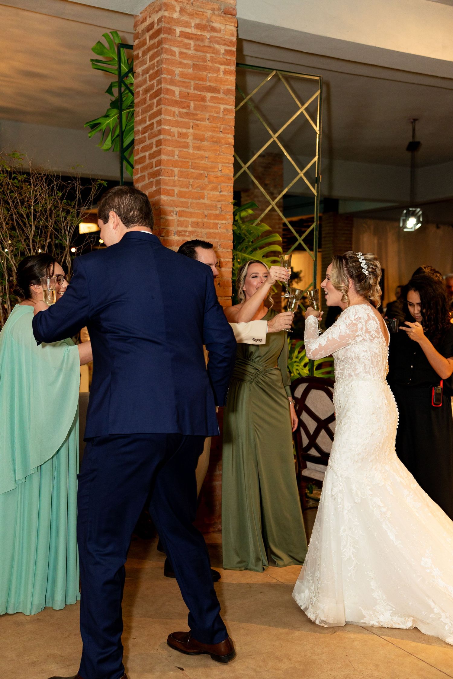 Bride in lace gown and groom in navy suit celebrate with guests at elegant wedding reception venue.
