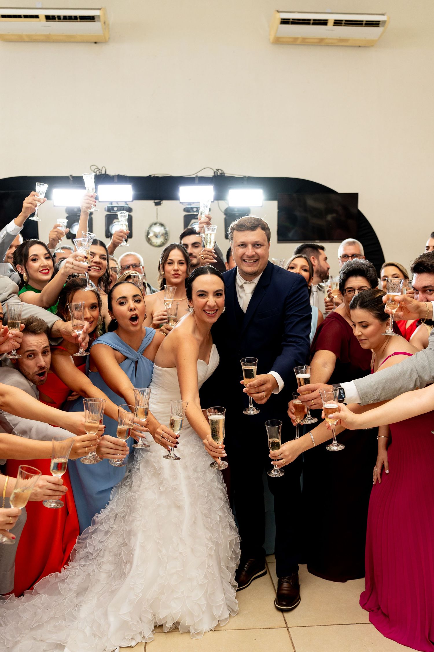 Bride and groom toast with champagne surrounded by wedding guests in formal attire at a festive indoor reception.