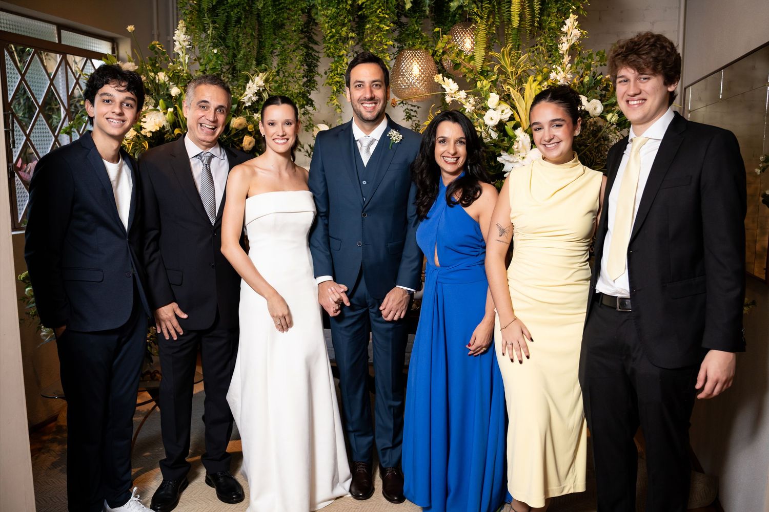 Seven elegantly dressed wedding guests posing and smiling together at a reception venue.
