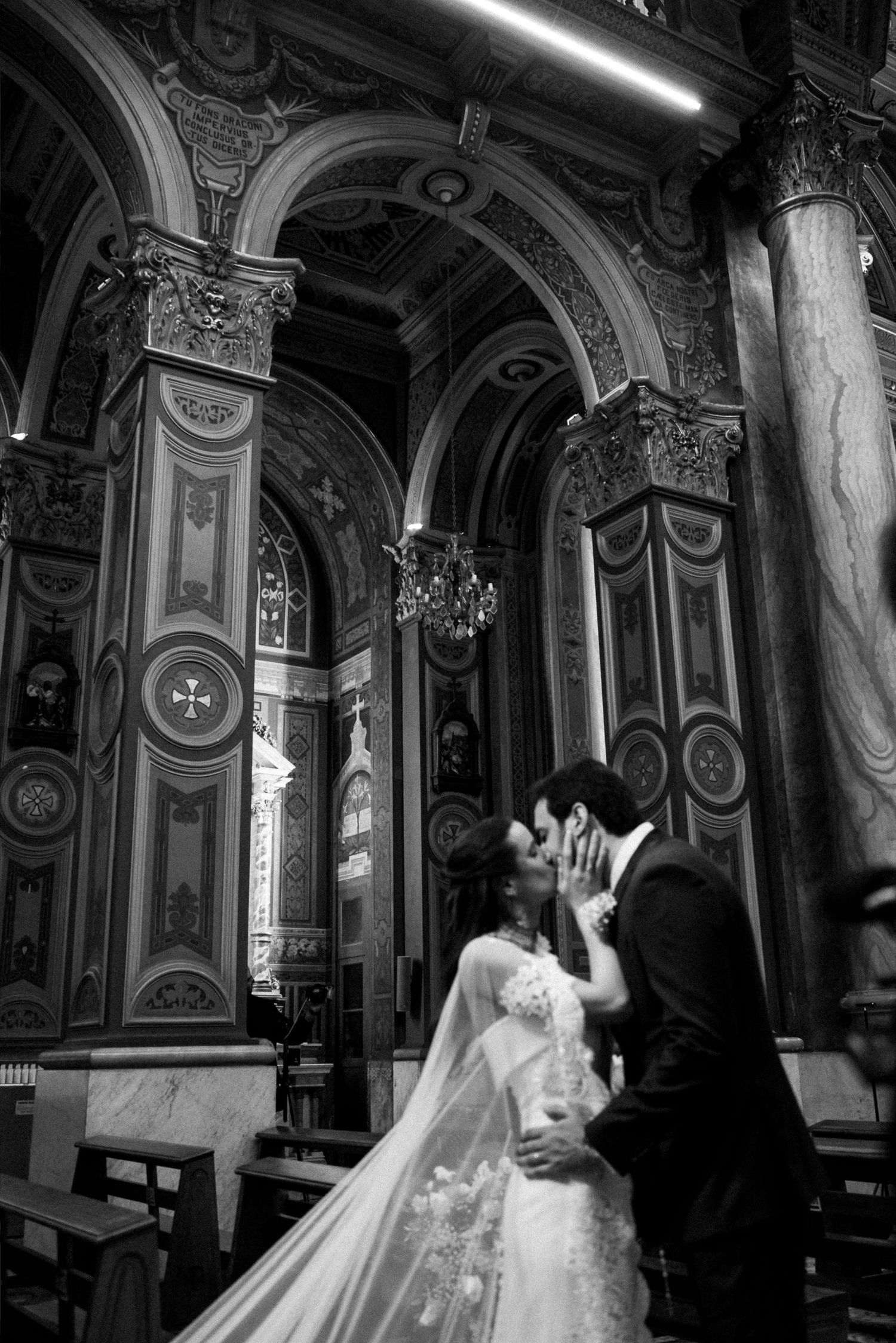 Black and white photo of a bride and groom sharing a kiss inside an ornate historic church.