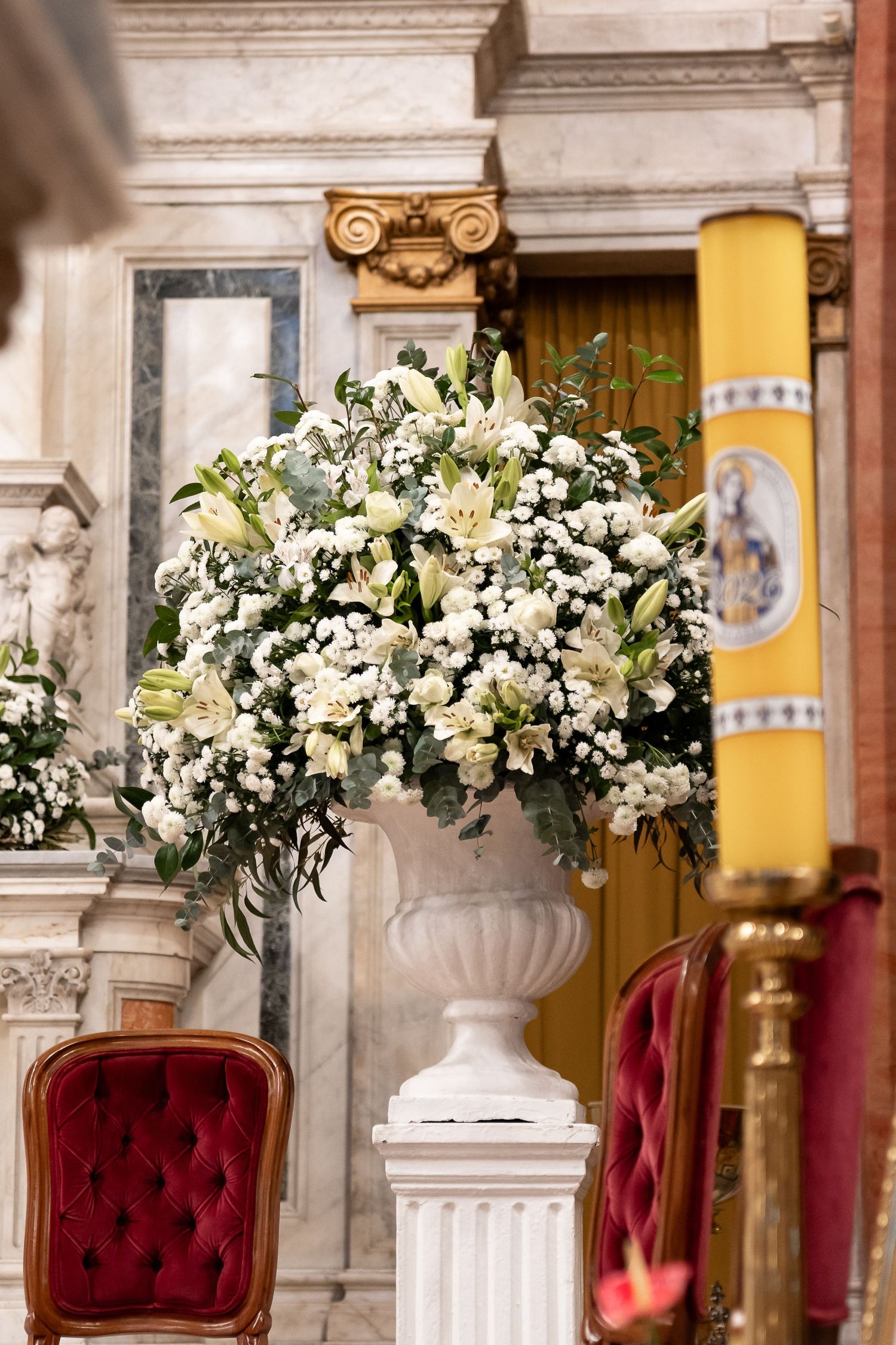 Elegant white floral arrangement in a classic urn vase on a pedestal inside an ornate marble church.