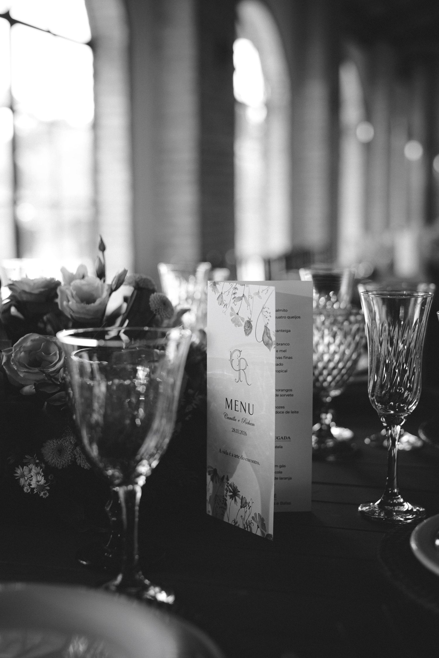 Black and white wedding table setting with crystal glasses, floral centerpiece, and elegant menu card.