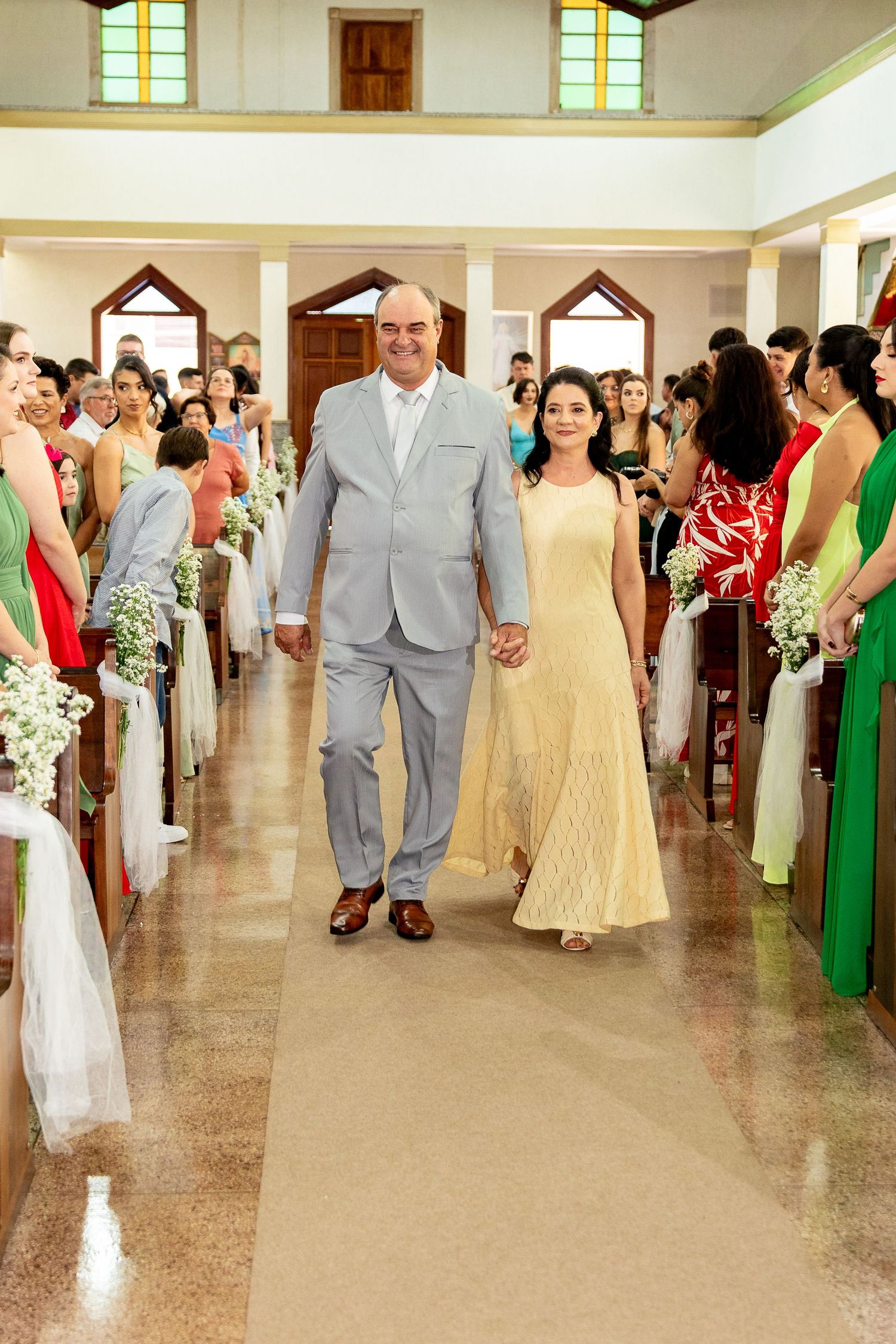 Couple walks down church aisle at wedding ceremony, man in gray suit, woman in yellow gown, guests seated in pews.