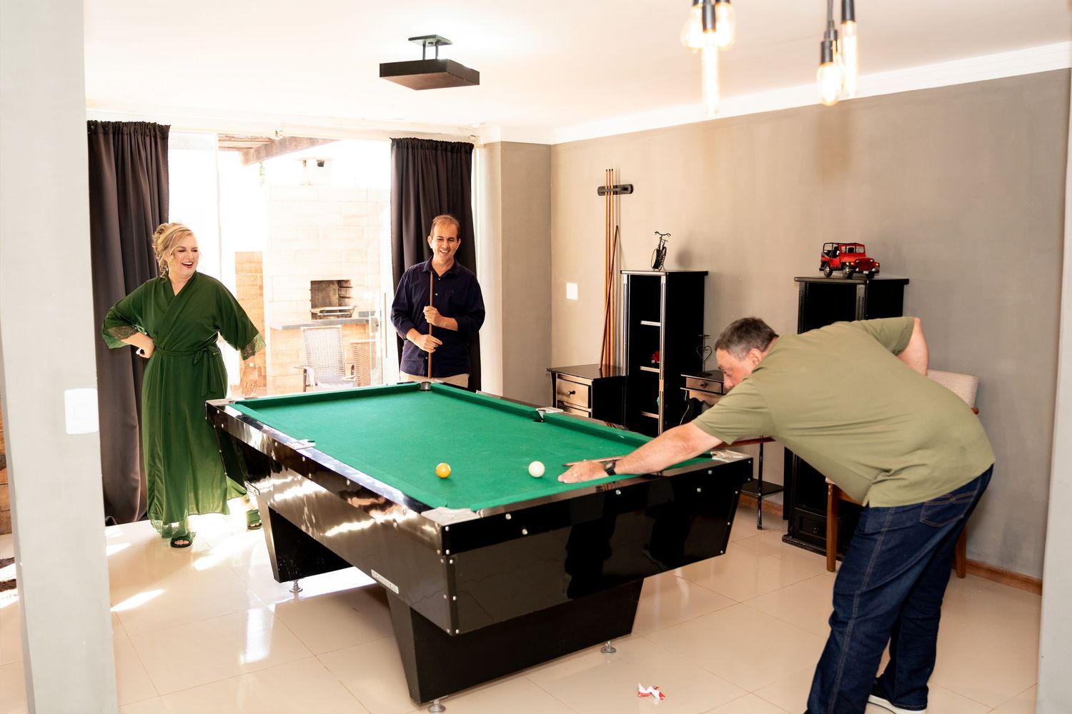 Three people enjoying a game of pool in a modern game room with a black billiard table and green felt.