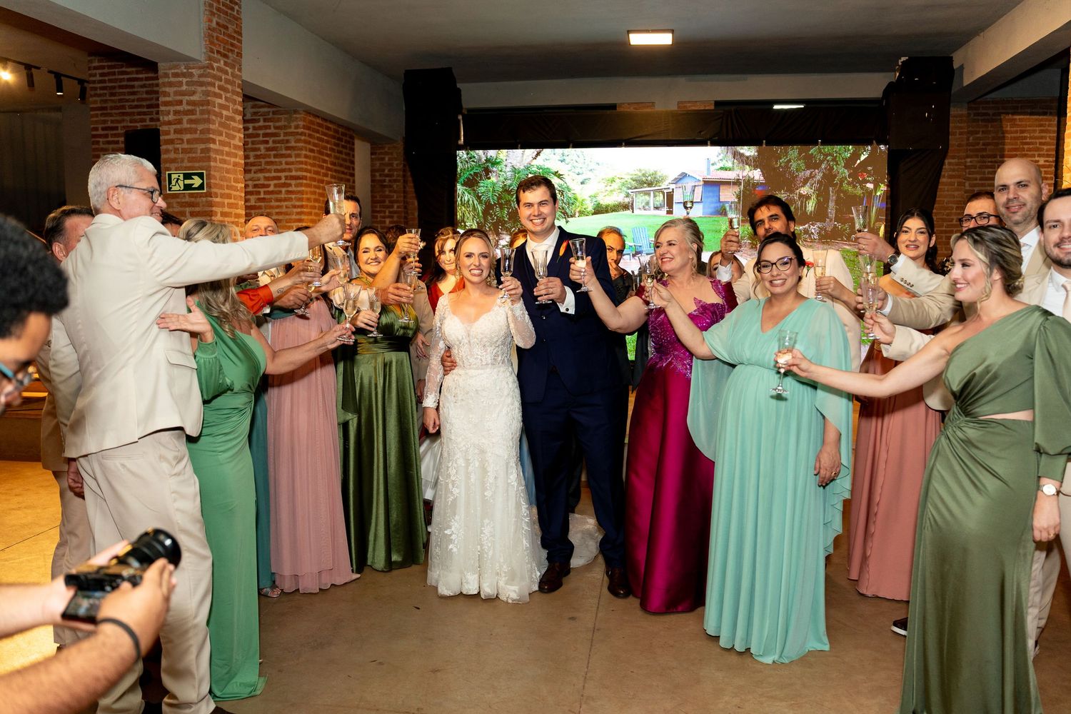 Bride and groom celebrate wedding entrance surrounded by guests in colorful bridesmaid dresses raising glasses in toast.