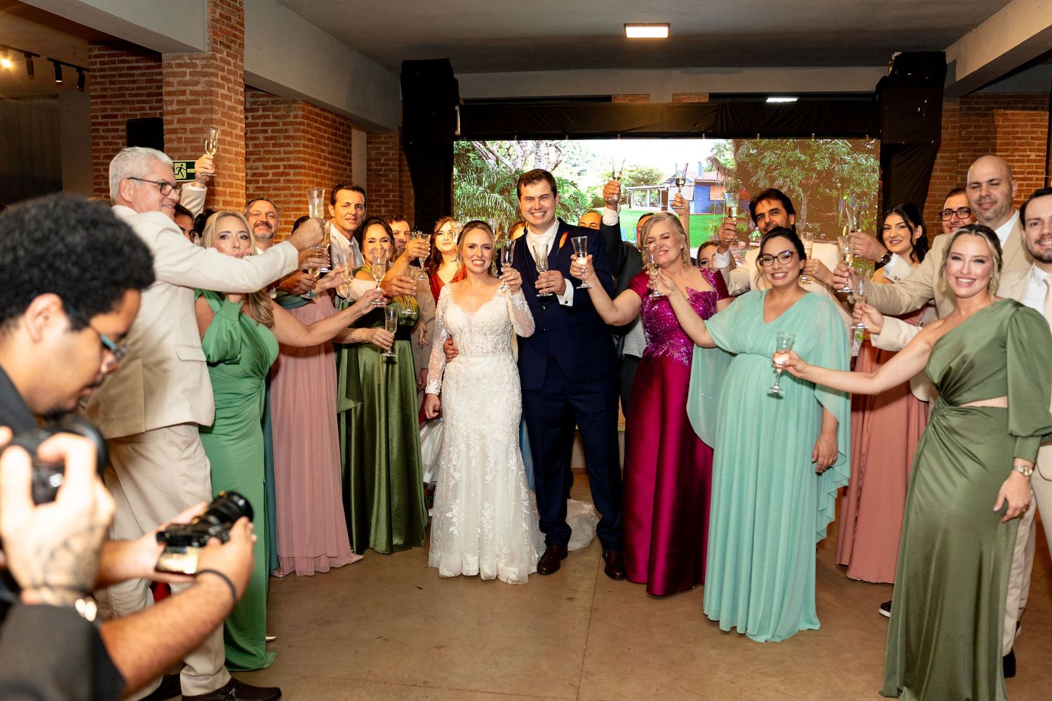 Bride and groom celebrate wedding reception entrance surrounded by guests in colorful formal attire raising glasses.