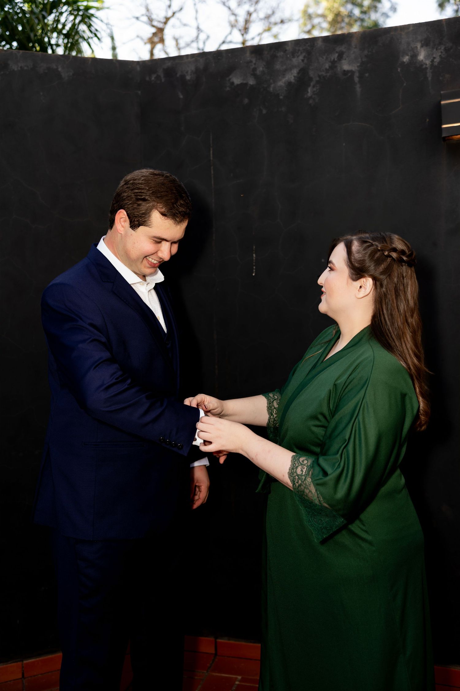 Couple in formal attire sharing a tender moment, man in navy suit and woman in green dress holding hands outdoors.