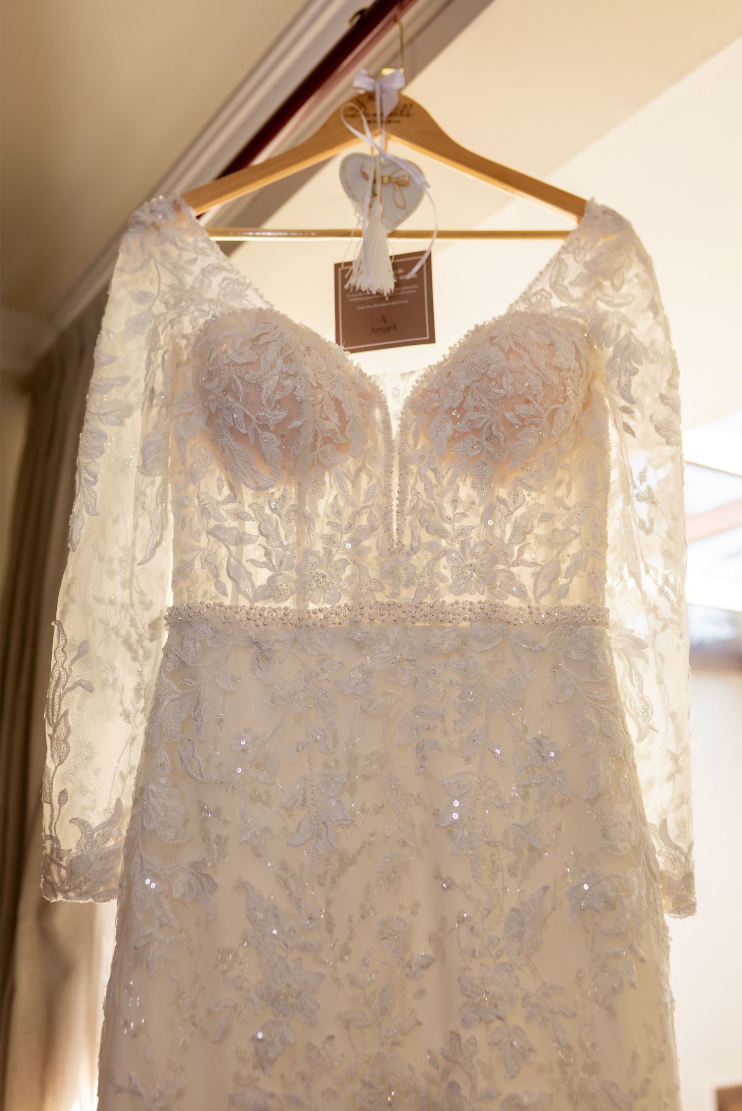 Elegant lace wedding dress with long sleeves and sweetheart neckline hanging on a wooden hanger.