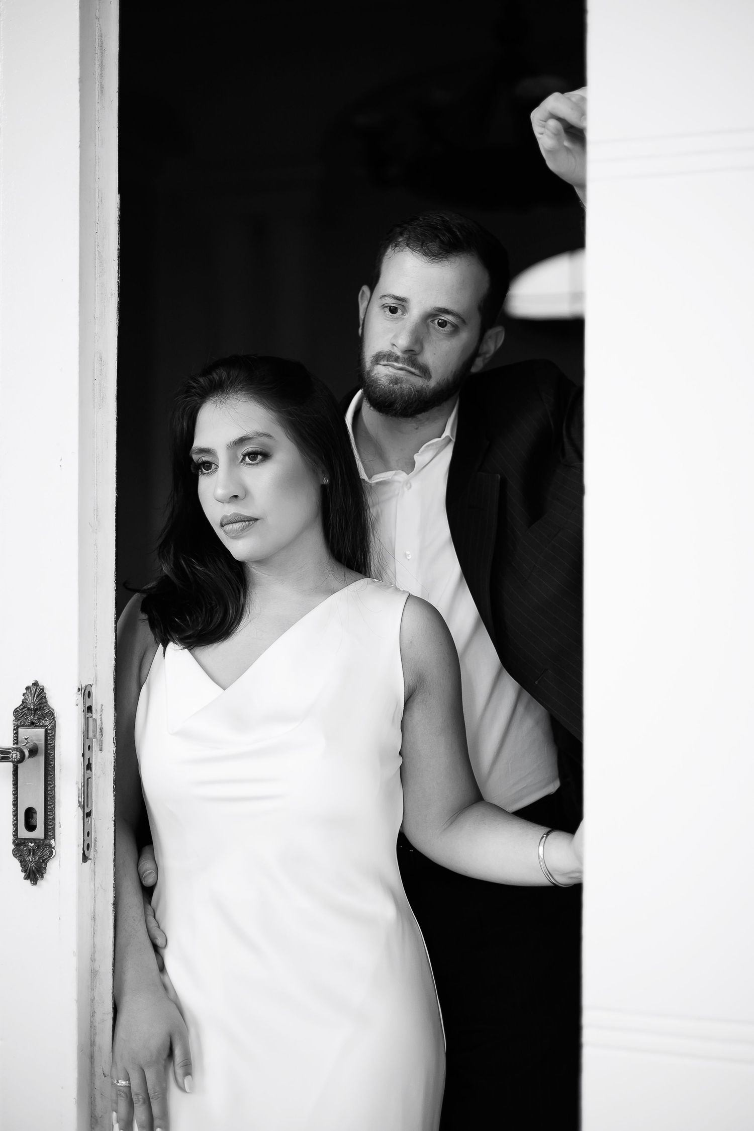 Black and white photo of a bride in white dress and groom in suit posing elegantly in a doorway.