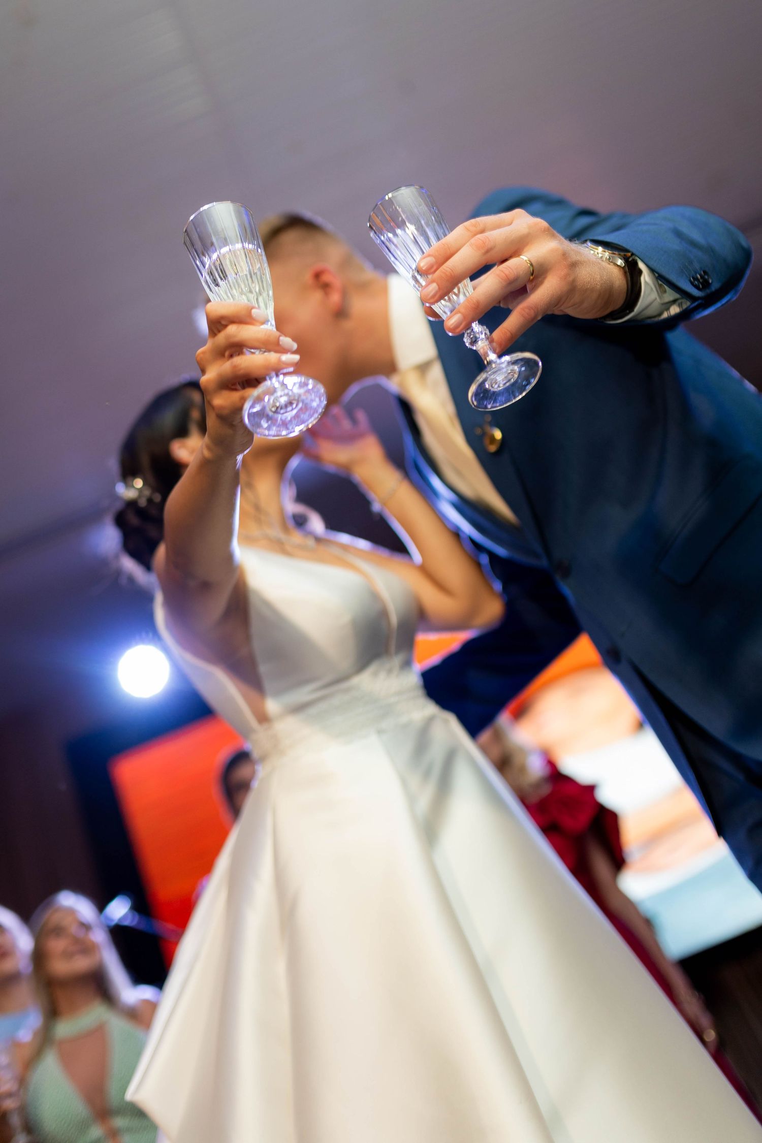 Bride and groom kissing while raising crystal champagne glasses at their wedding reception celebration.