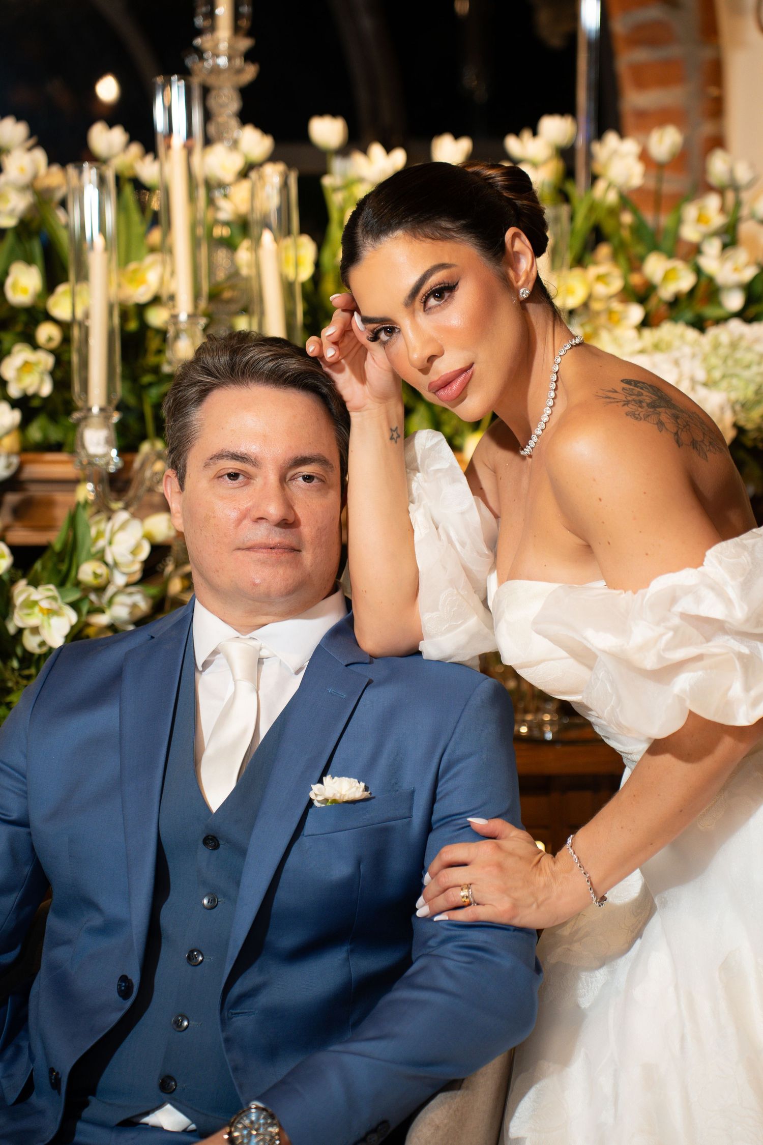 Elegant bride and groom posing together at wedding reception with white tulips and candles in background.