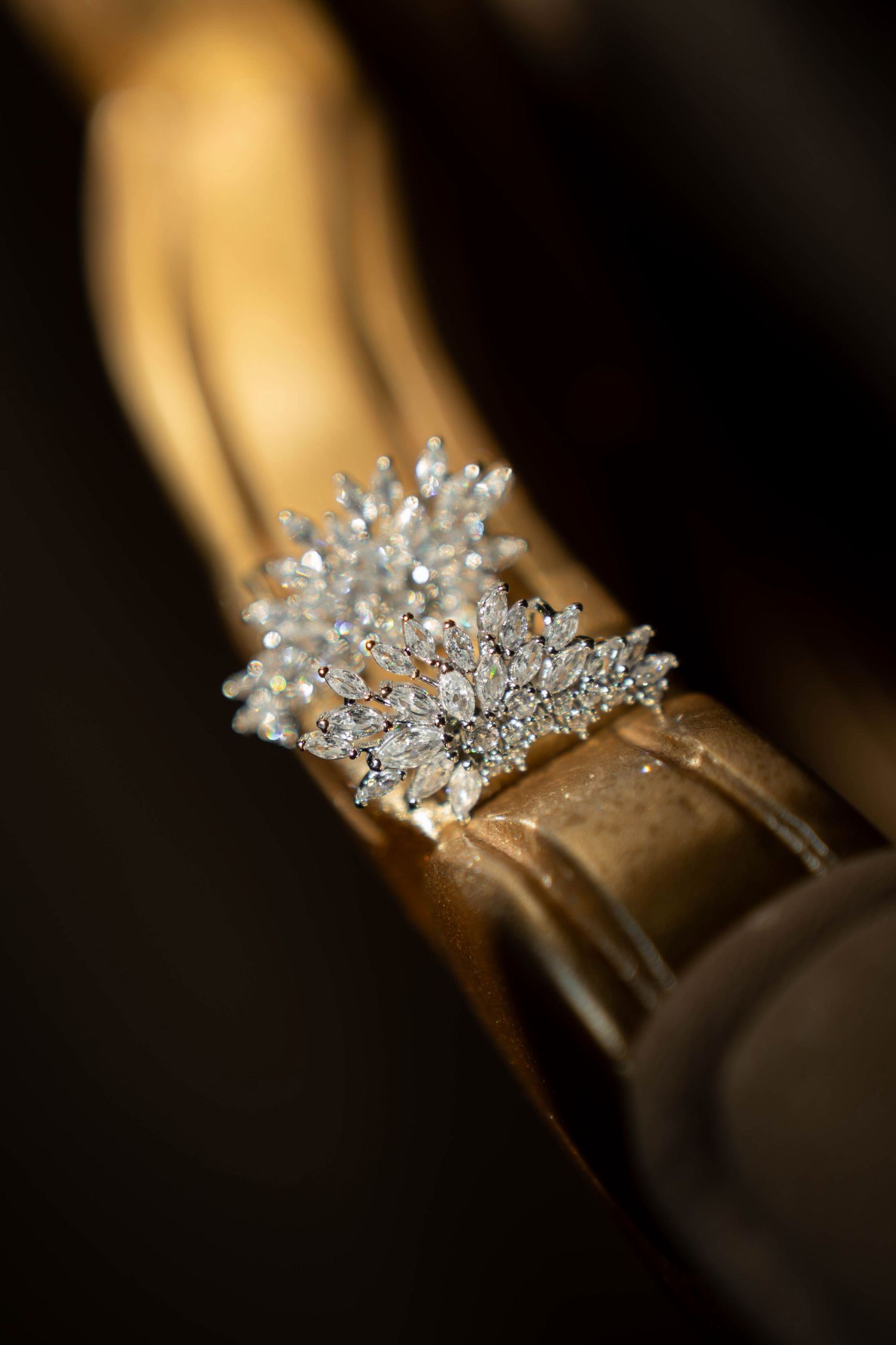 Elegant diamond cluster ring displayed on a golden surface, featuring sparkling marquise and round cut stones in a floral design.