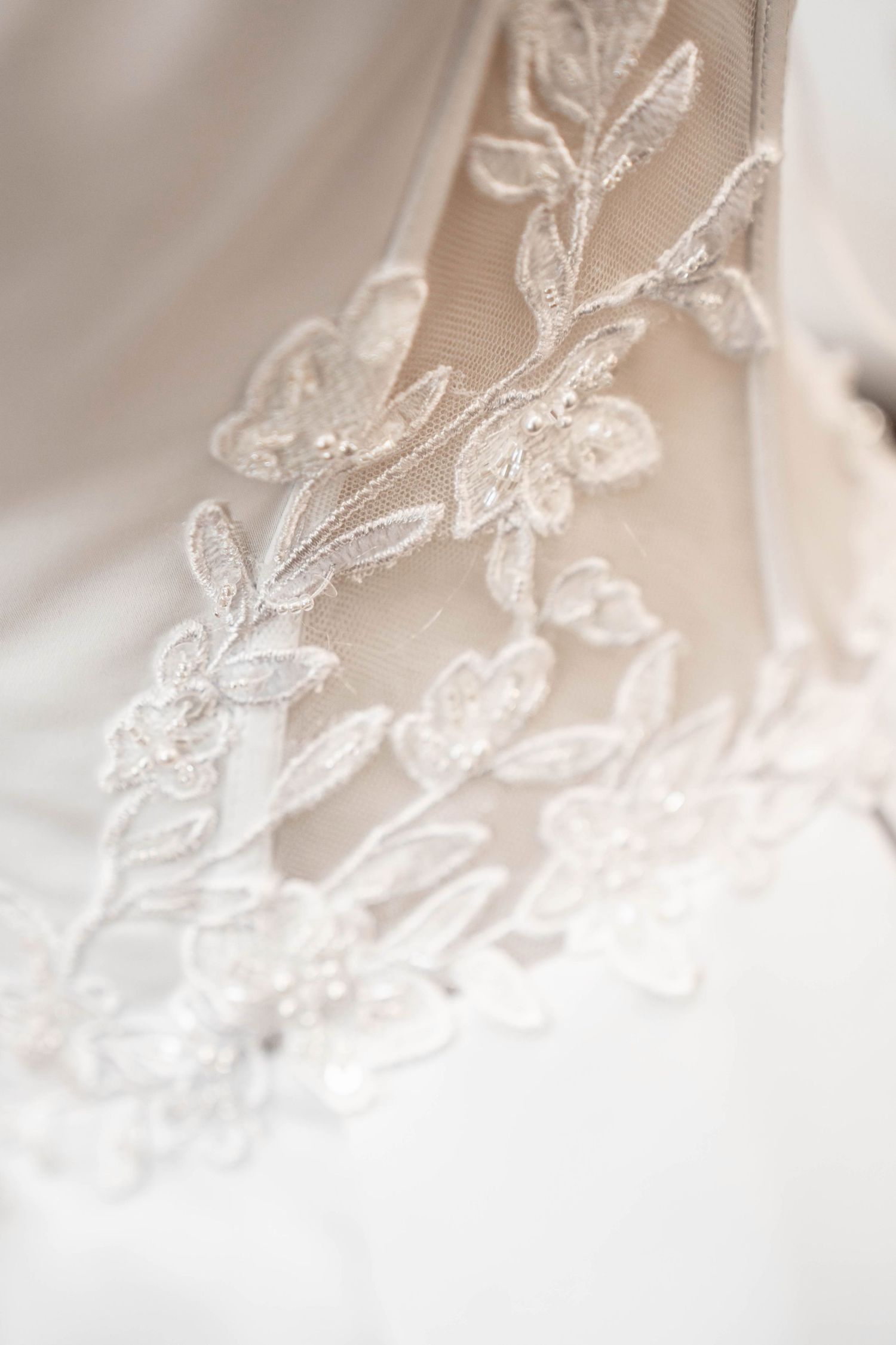 Close-up of delicate white floral lace embroidery with pearl beading on a bridal wedding gown veil.
