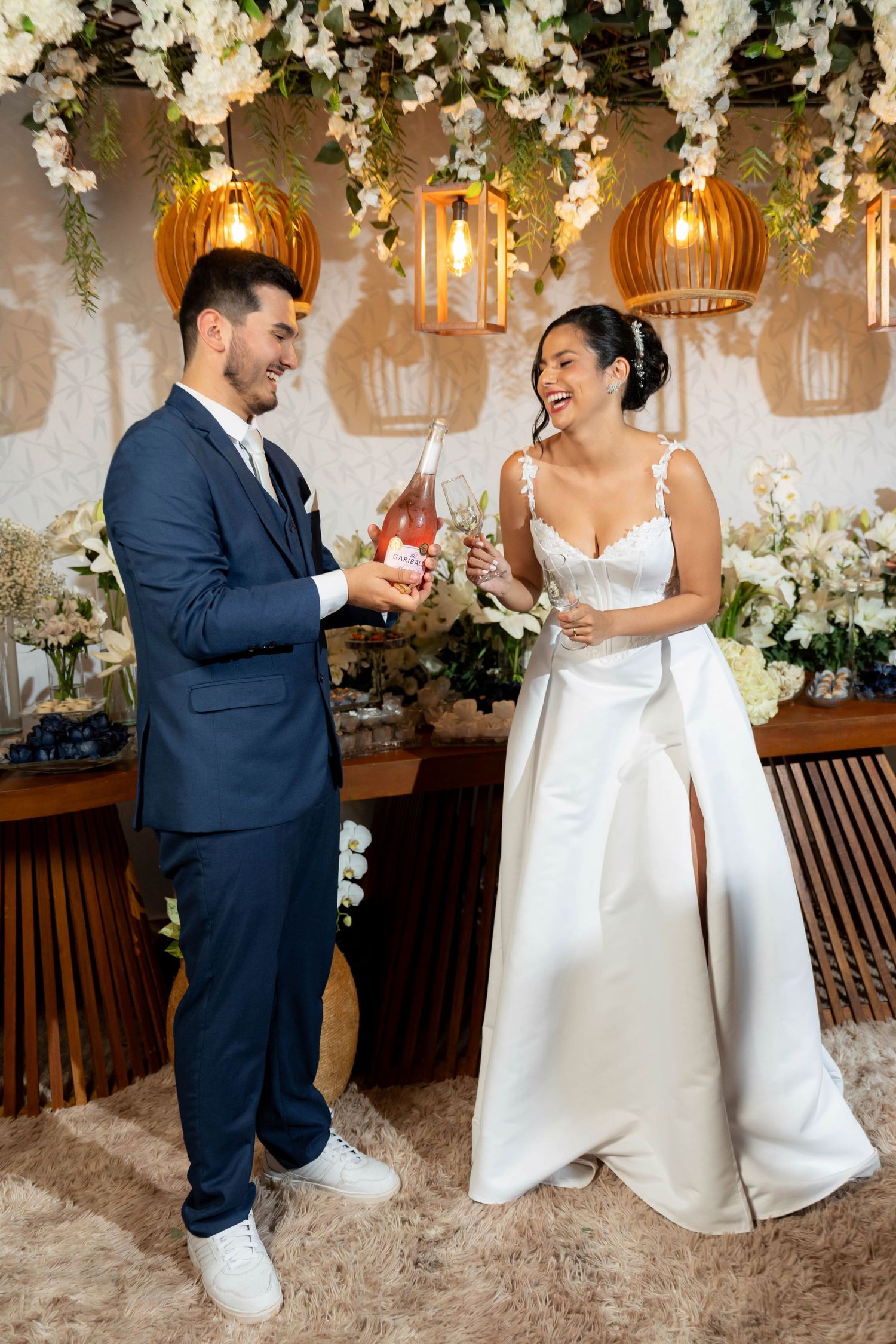 Bride and groom laughing while pouring champagne at their elegant floral wedding reception.