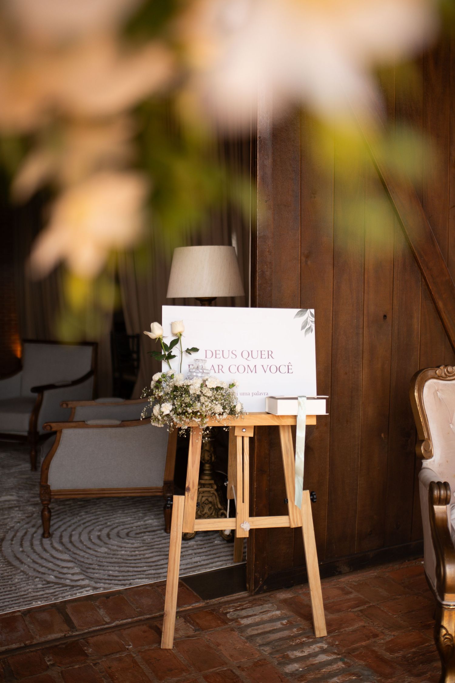 Wooden easel with floral arrangement and Portuguese wedding sign in elegant rustic venue setting.