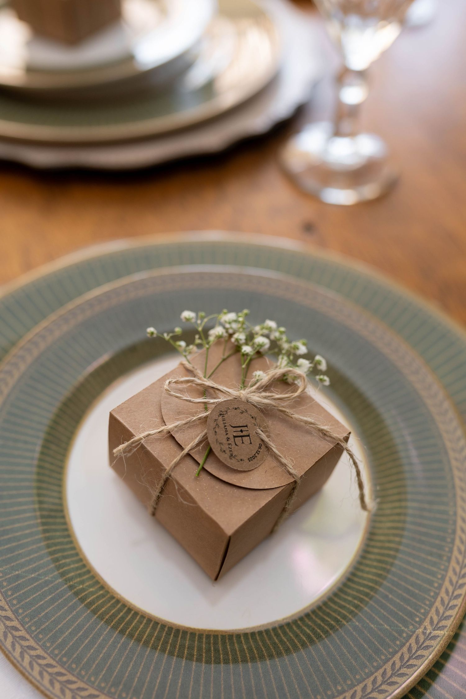 Elegant kraft paper wedding favor box tied with twine and baby's breath on a sage green plate.