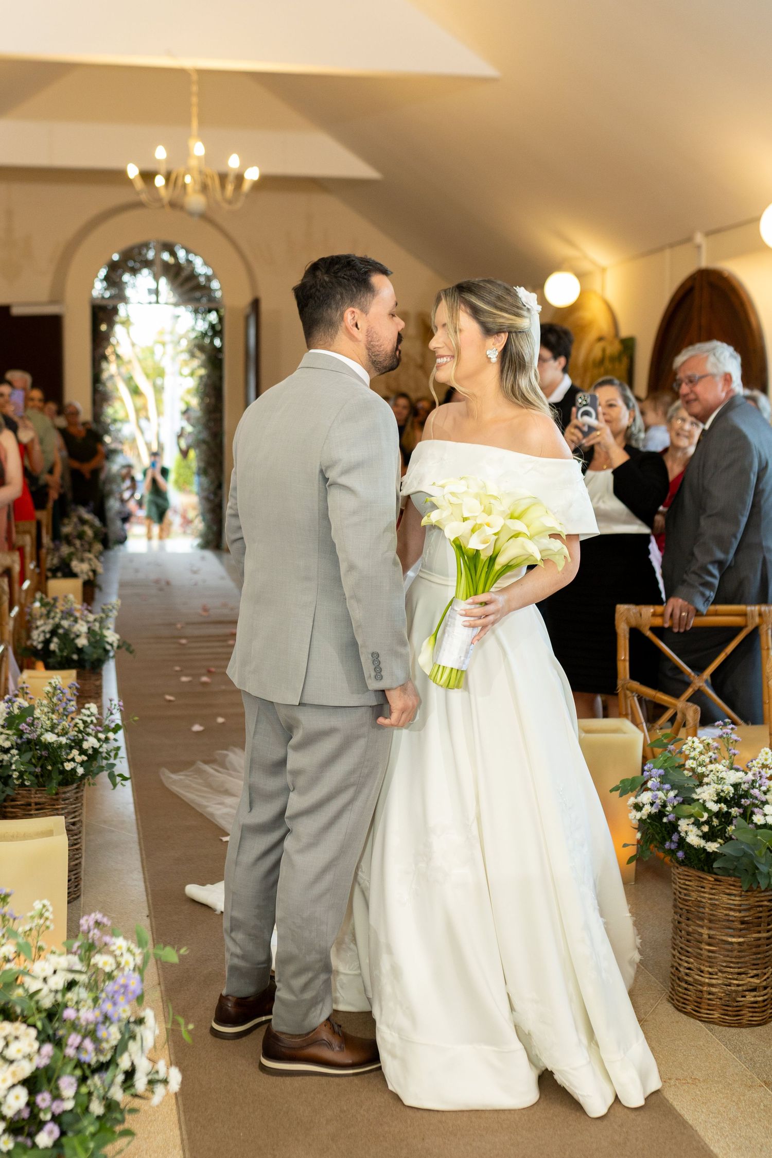 Bride and groom share a romantic moment at the altar, she holds white calla lilies bouquet in a chapel ceremony.