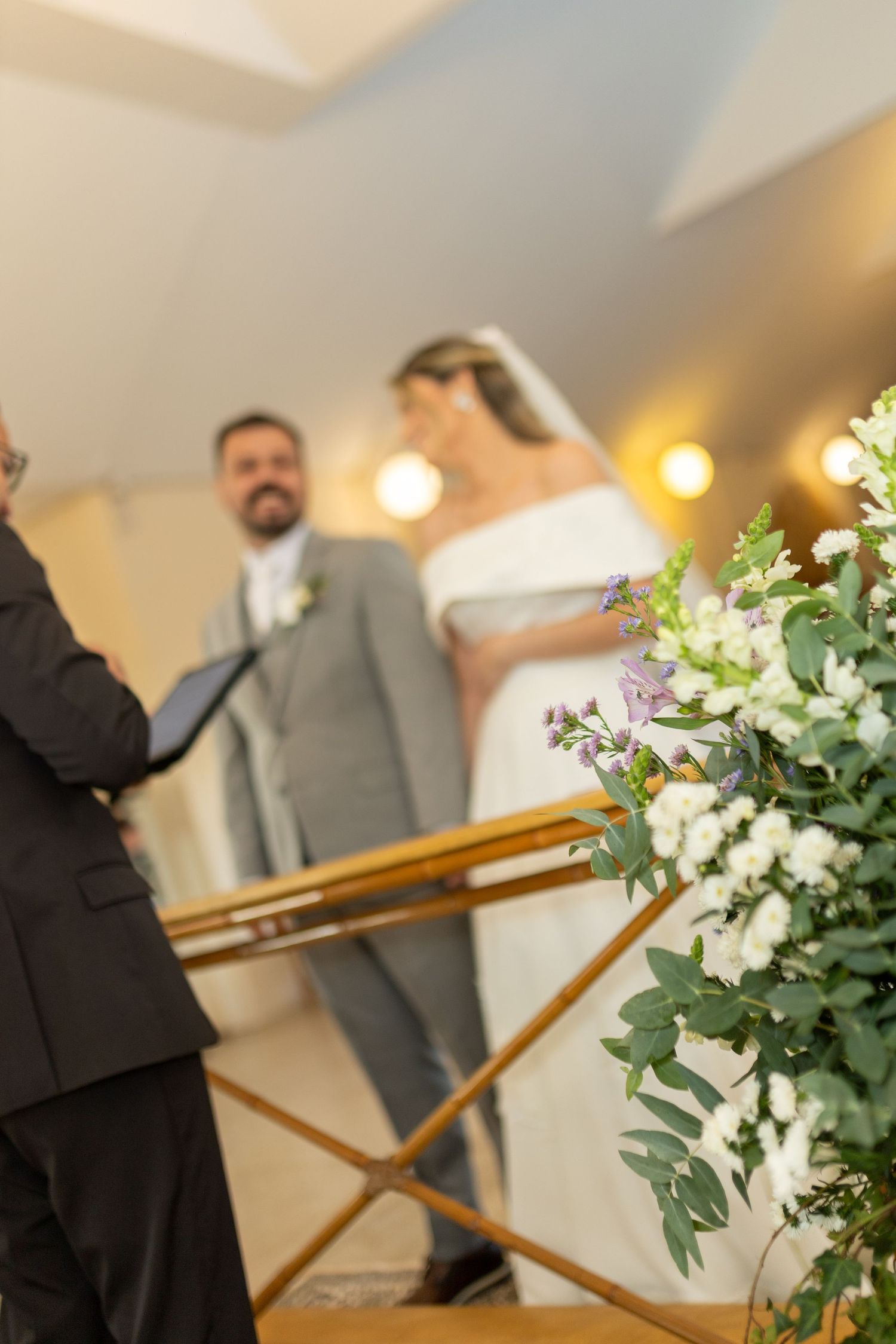 Bride and groom stand at the altar during wedding ceremony with elegant white floral arrangements in the foreground.