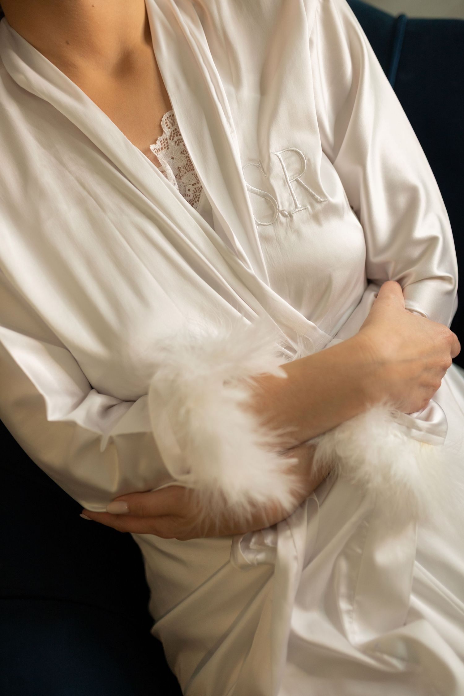 Bride in white satin monogrammed robe holding a fluffy white bouquet accessory on her wedding day.