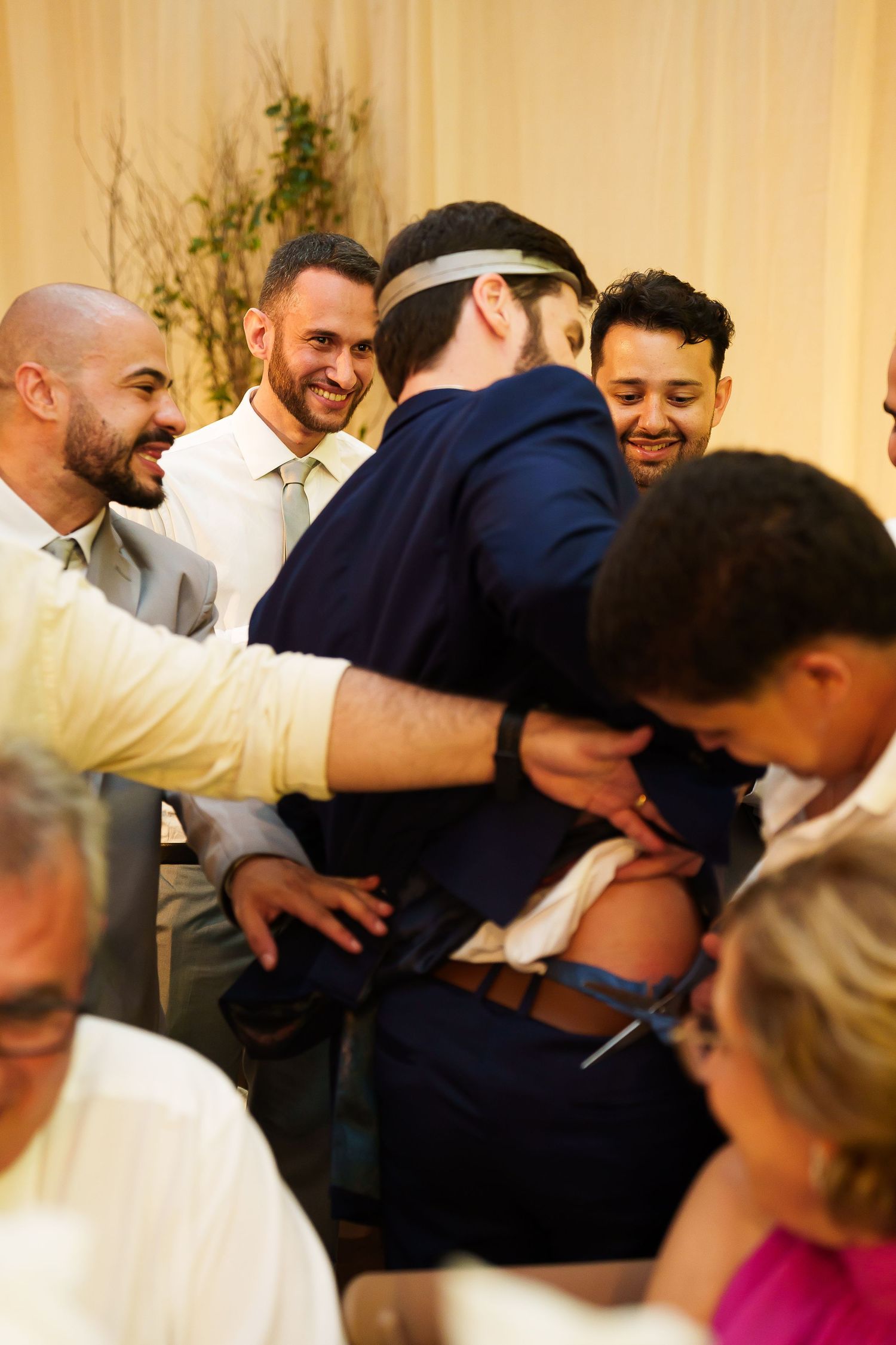 Group of smiling men in suits celebrating at a wedding reception, gathered closely together in a festive moment.