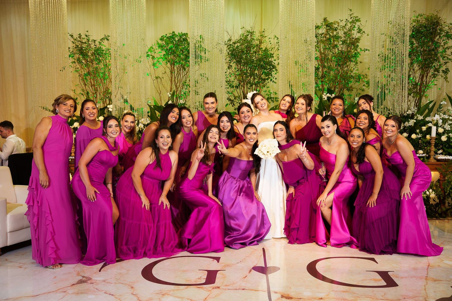 Bride in white gown surrounded by bridesmaids in fuchsia dresses on decorated dance floor with monogram G.