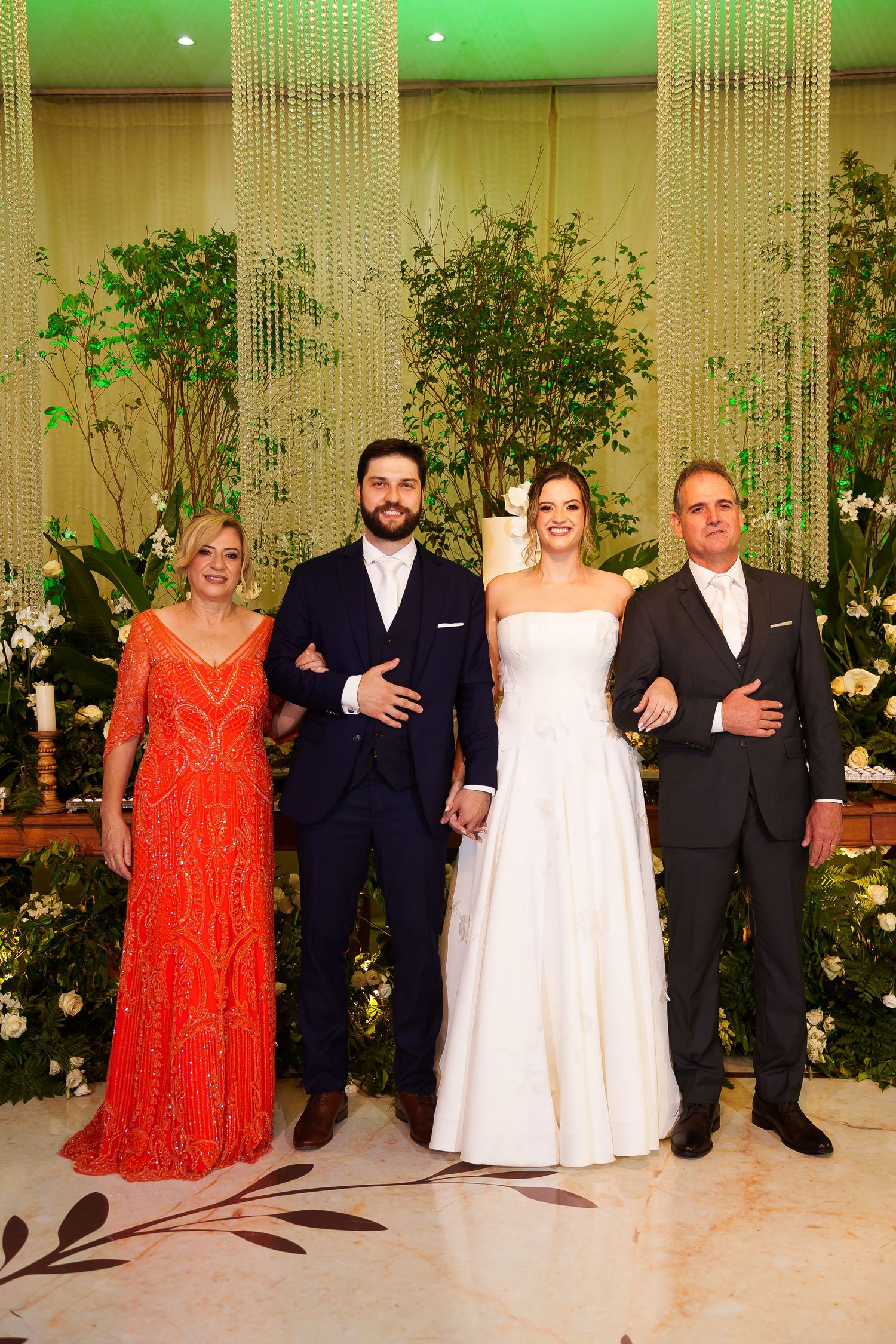 Wedding party of four posing elegantly, bride in white gown, groom in navy suit, flanked by family in formal attire.