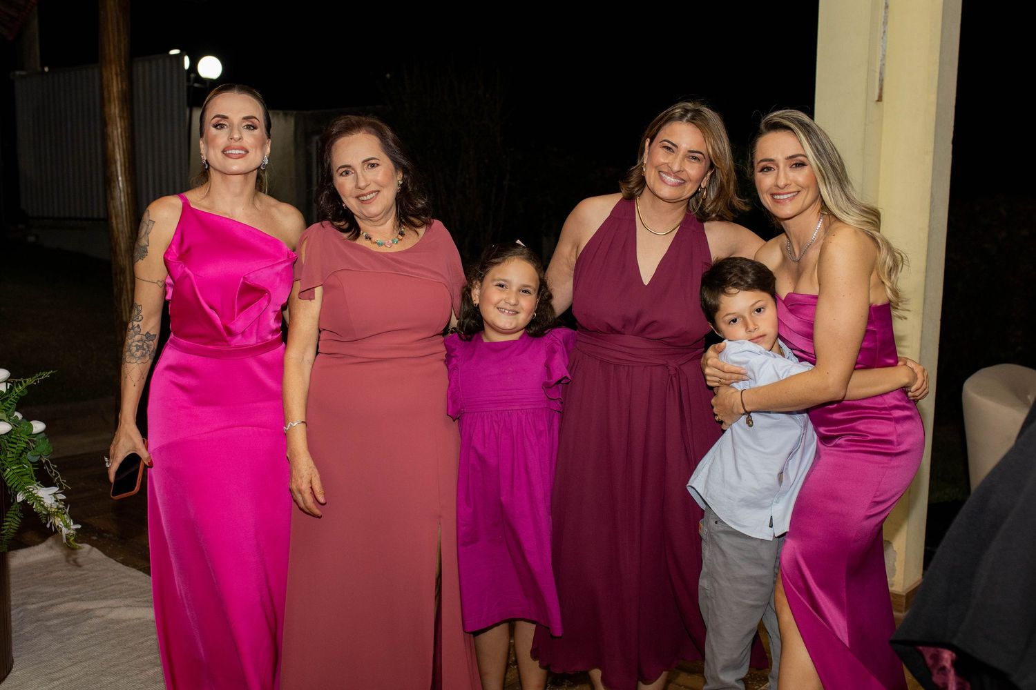 Group of women and children in pink and magenta formal dresses posing together at an evening event.