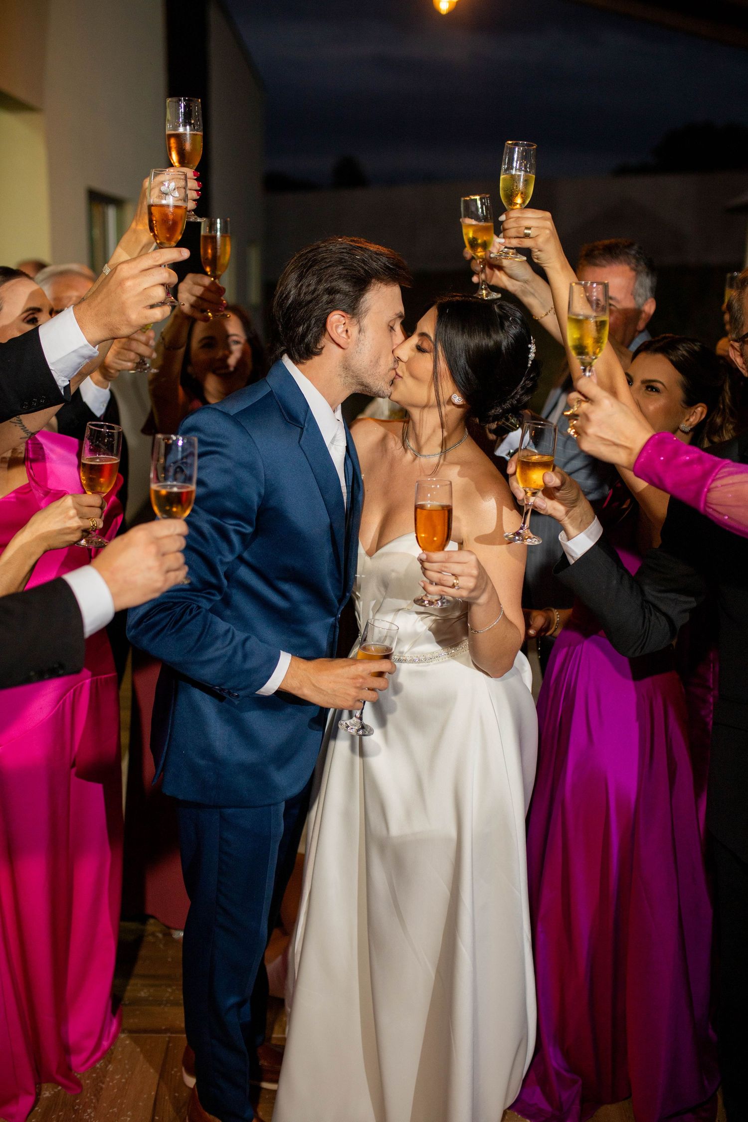 Bride and groom kissing while guests raise champagne glasses in a wedding celebration toast.
