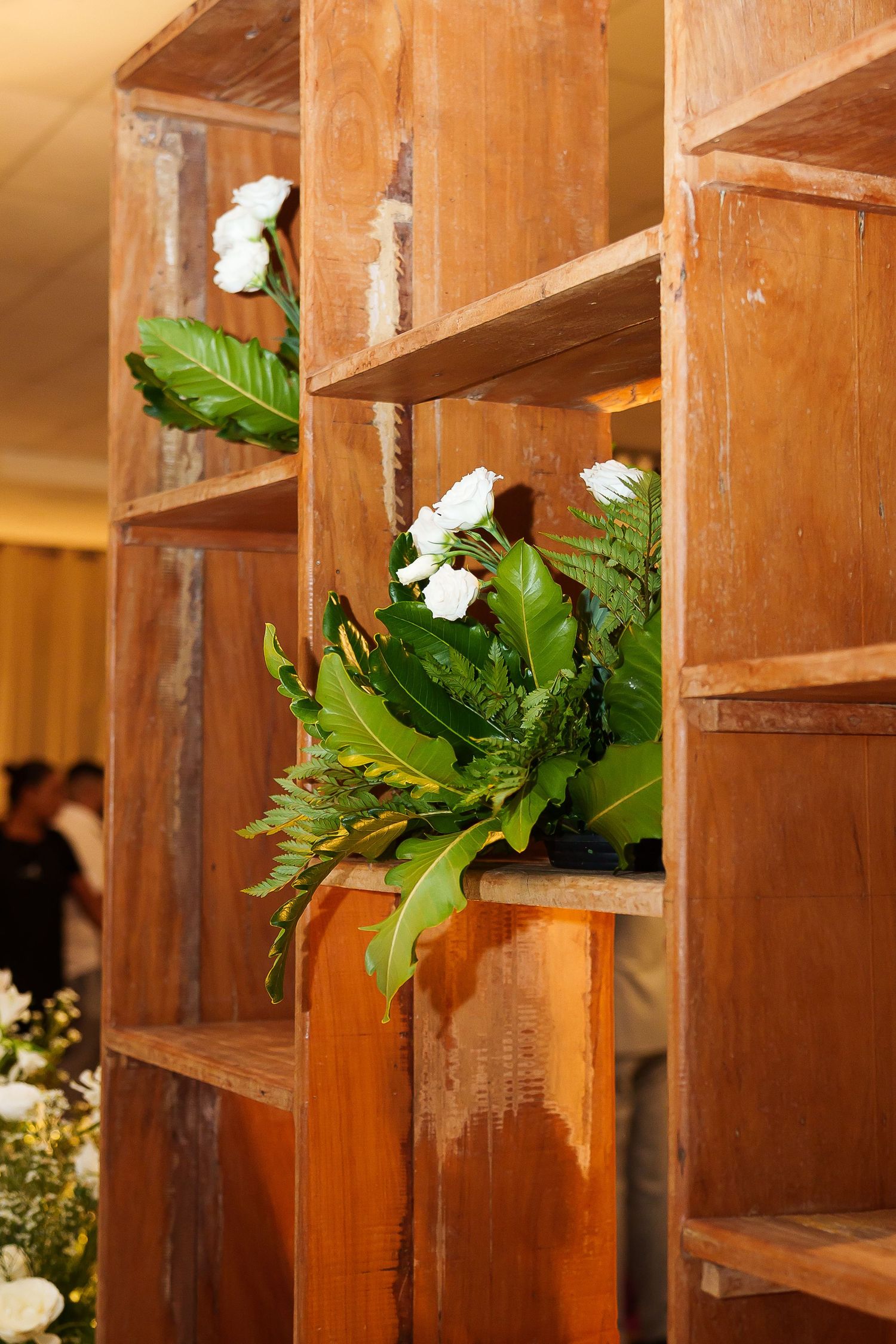 Rustic wooden shelving unit decorated with white carnations and lush green ferns at an elegant event.