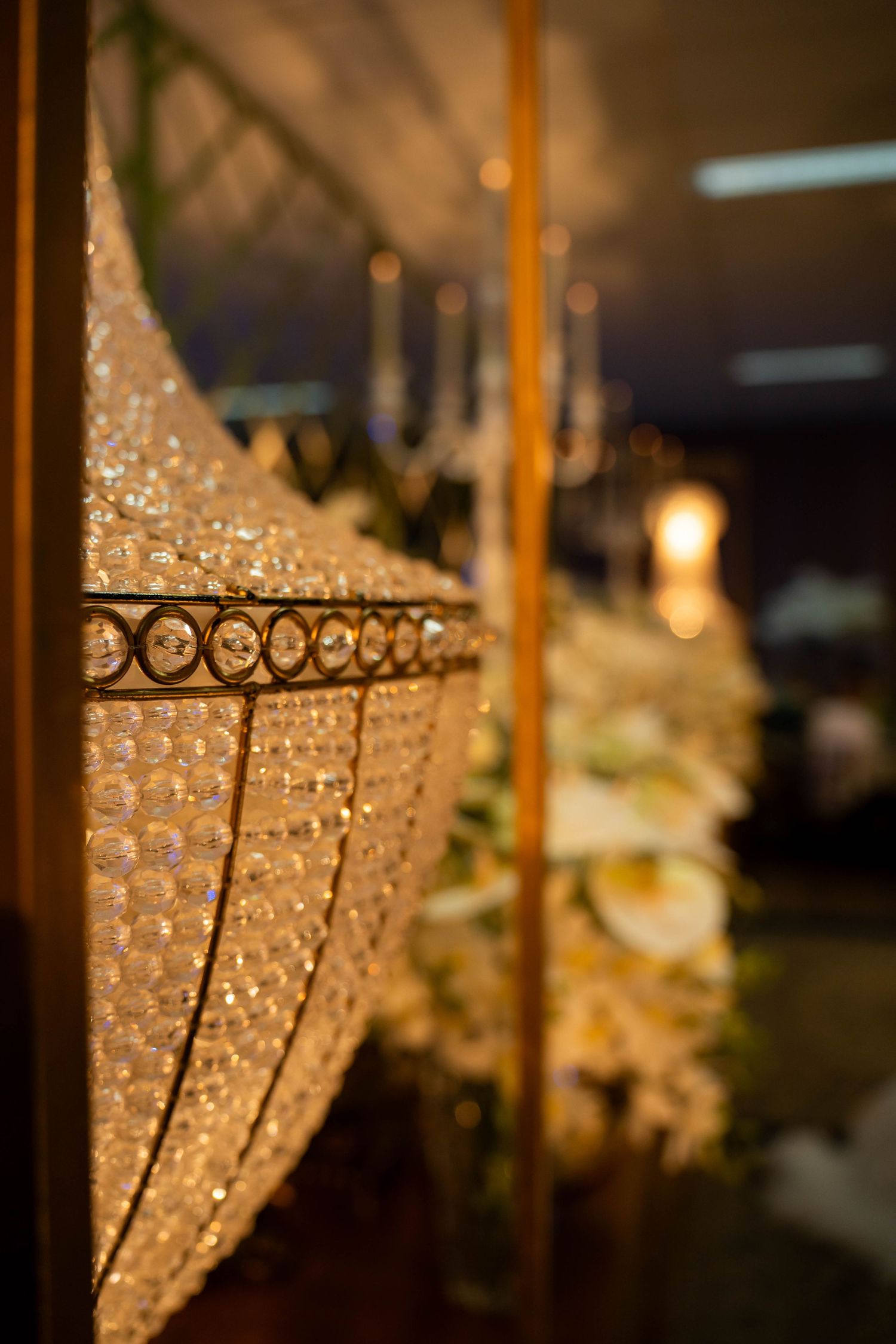 Close-up of an elegant crystal chandelier with golden accents at a formal event venue with floral decor.