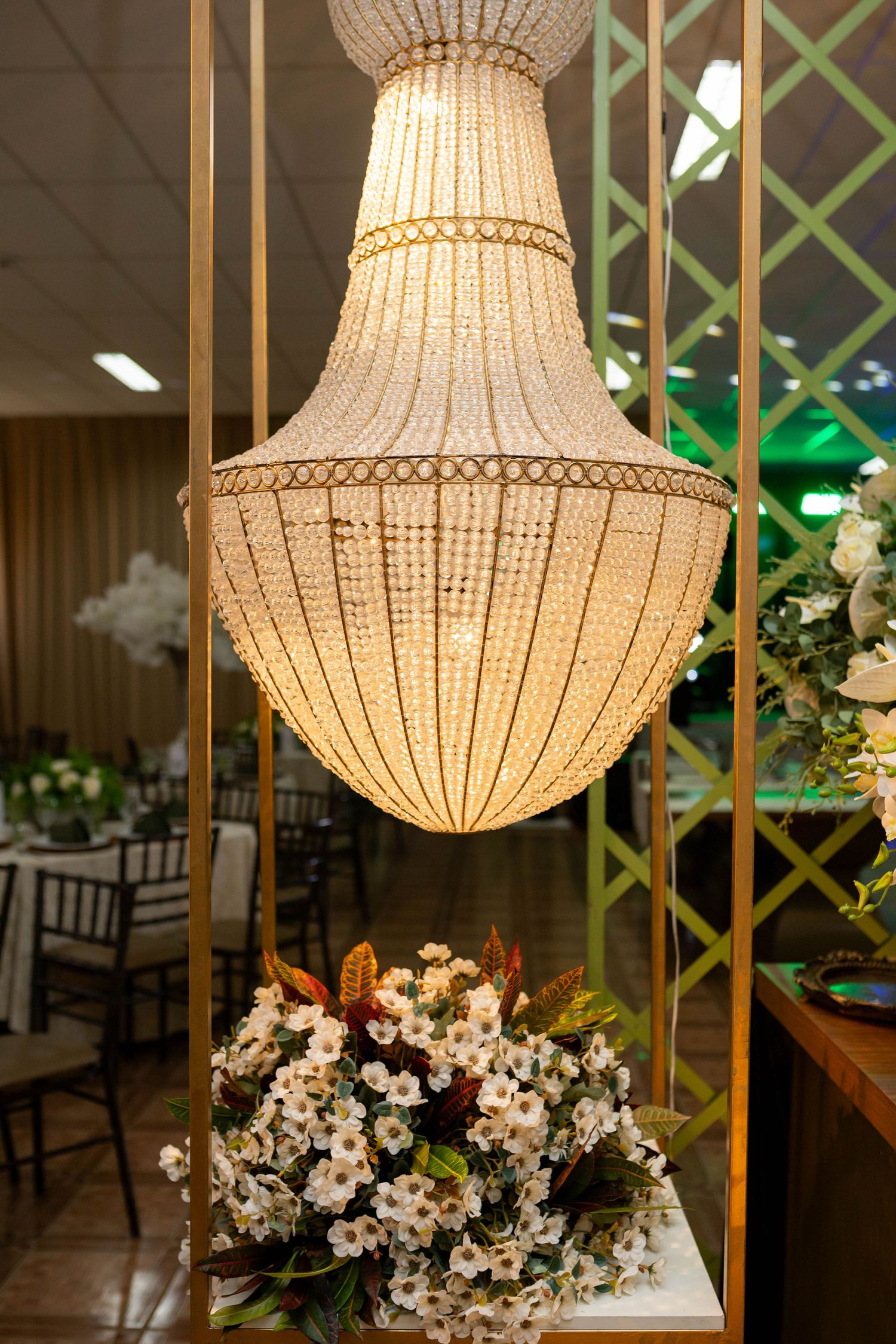 Elegant crystal chandelier hanging above a white floral arrangement in a decorated event venue.