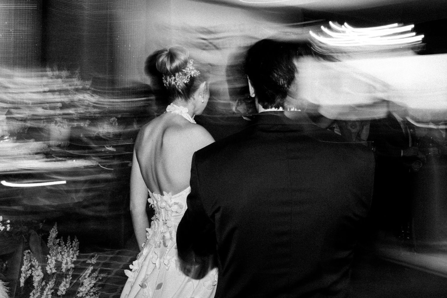 Black and white motion blur photo of bride in backless gown dancing with groom at wedding reception.