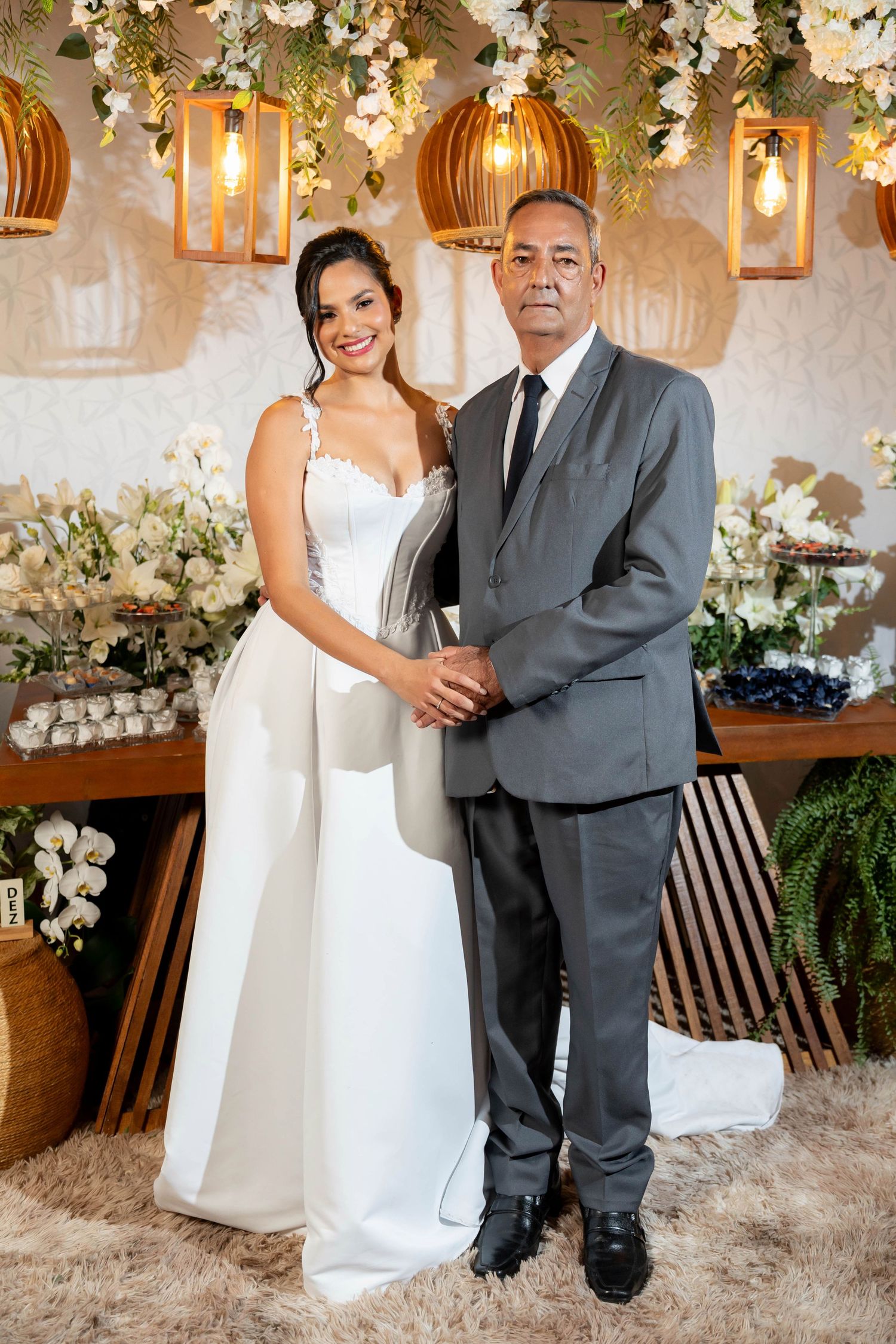 Bride in white gown and groom in gray suit pose together at elegant wedding reception with floral decor and warm lighting.